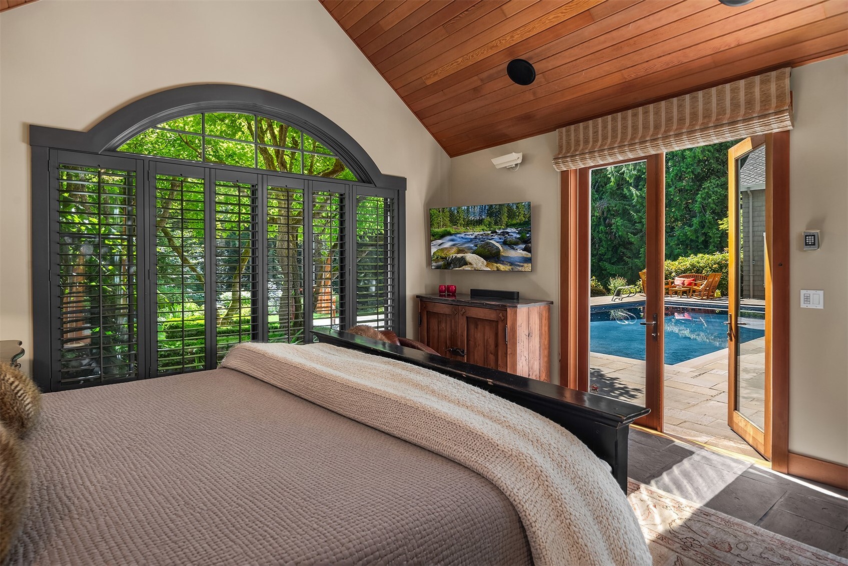 Bedroom with arched shuttered window, wall-mounted TV, and door to pool patio