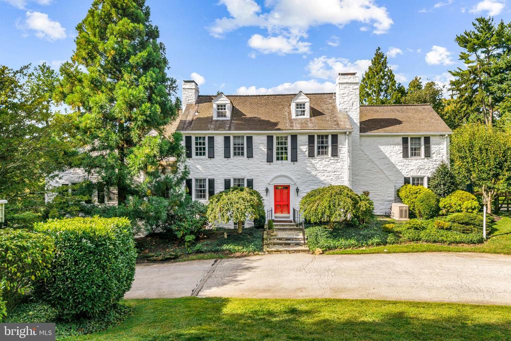 Surrounded by pastoral beauty and across from preserved land, this classic 1930s Main Line estate blends privacy with convenience in one of Gladwyne’s most desirable settings. The painted white stone exterior with black shutters captures timeless character on 2.47 acres with sweeping lawn and mature landscaping. 1324 Youngsford Road encompasses a main residence with 7,112 square feet on three levels—five bedrooms, five full and one half bath—along with a two-bedroom, two-bath carriage home. Combined home and carriage house offers 7 beds, 7.5 baths,The main level showcases  distinguished spaces, where old-world character meets architectural detail. A slate walkway with wrought-iron railing leads to the front entry, opening to a foyer that introduces gracious gathering rooms. Straight ahead, the dining room is framed by a wide triple window, creating a beautiful setting for formal dining. To the right, the living room impresses with wide-plank hardwood floors, soaring ceilings, and a paneled fireplace surround that reflects the home’s craftsmanship. French doors open to a side slate terrace with a stone sitting wall overlooking the pool and gardens, while expansive windows and doors throughout this level flood the rooms with natural light. From the living room, two openings connect to the striking family room addition by renowned builder E.B. Mahoney. Distinguished by generous proportions, hardwood floors, and a wall of windows, this light-filled space is the heart of the home. A second fireplace adds warmth, while French doors extend the living space outdoors. A hall off this room houses a three-stop elevator serving the lower level and primary suite. A cozy sitting room with built-ins and the home’s third fireplace provides an intimate retreat, while a powder room is conveniently placed off the foyer. The sunny kitchen offers three windows, a side door, and an adjoining breakfast nook with a bay window for casual meals. This wing also includes an office, laundry room, full bath, and rear staircase. While functional, these spaces offer opportunities for customization or a more open layout.Upstairs, the expansive primary suite spans an entire wing with a spacious bedroom, walk-in closets with built-ins, and a sitting room that can serve as a home office or quiet retreat. The en-suite bath includes a large vanity and water closet, with space for updating. Bedrooms two and three share a Jack-and-Jill bath, while bedroom four enjoys its own en-suite bath and walk-in closet. The third floor features a fifth bedroom with en-suite bath—ideal for a guest or Au pair suite. All bedrooms are carpeted, with hardwood flooring underneath awaiting refinishing.The walk-out lower level offers a recreation room with slate floors, panelled walls, beamed ceilings, a bar, and the home’s fourth fireplace. French doors open to a slate patio and the rear yard, providing access to the pool and gardens for entertaining. Storage areas, utilities, and interior access to the side-entry two-car garage complete this level.A separate carriage house provides 1,581 square feet of flexible space with living, dining, kitchen, bedroom, and full bath on the main level, plus a second bedroom and bath upstairs. Ready for cosmetic updates, it offers versatility for guests, in-laws, or business use, supported by the property’s license. Outdoor amenities include a pool with patio and greenery, a stone pool house, and expansive lawns with mature landscaping that create a picturesque setting.With timeless architecture, distinguished spaces, and strong bones to be re-imagined, this is a rare opportunity to own a standout home in one of Gladwyne’s most coveted settings. Just half a mile from the Village of Gladwyne and close to Kenealy Nature Park, the Bridlewild Trail, and award-winning Lower Merion schools, the property offers both tranquillity and accessibility. Narberth Station is three miles away with service to Philadelphia and New York.