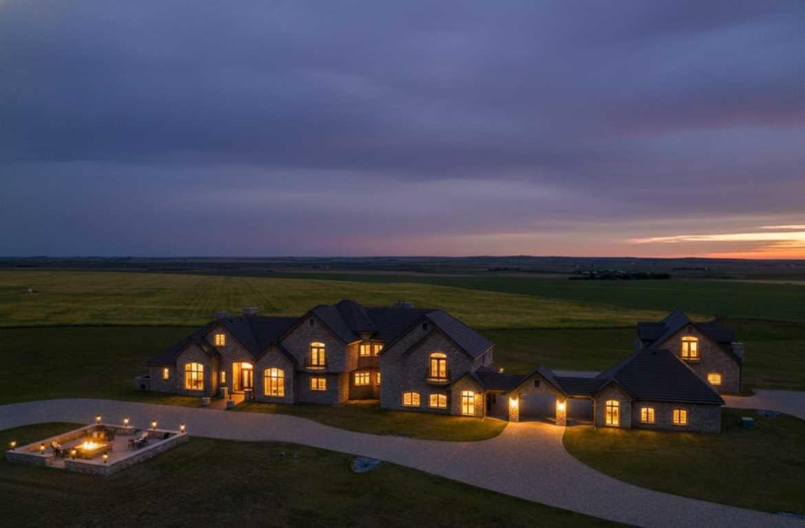 160 Acres of Prairie Elegance – A Landmark Estate of Luxury, Scale, and PossibilityWelcome to an extraordinary 160-acre estate in the heart of Alberta’s Kneehill County—a rare offering where timeless craftsmanship meets the quiet beauty of prairie living. Just one hour from Calgary and YYC International Airport, this estate combines luxury, privacy, and flexibility, making it ideally suited for multigenerational living, a boutique retreat, or a distinguished rural residence unlike any other.At the heart of the property is a magnificent 13,000+square foot stone-clad home, thoughtfully designed and masterfully built with uncompromising attention to detail. From the rich cherry oak mouldings and custom cabinetry to the Cheryl Wagner gold hardware and fixtures, every finish is of the highest quality. The home's Crestron smart technology, soaring ceilings, and seven gas-lit wood-burning fireplaces create a setting that is as refined as it is welcoming.The layout is exceptionally spacious, designed to accommodate large-scale entertaining while maintaining a warm and livable flow. Each of the seven bedrooms includes its own private ensuite, and every room opens directly onto an outdoor patio, inviting the surrounding landscape into everyday life. A newly built enclosed solarium expands the indoor-outdoor living experience even further—offering a year-round space to relax, dine, or entertain while immersed in natural light and panoramic views.Wellness is a central theme in this home, with a private gym, steam room, and spa all located on the lower level. The chef’s kitchen is a showpiece, offering top-tier appliances, granite countertops, a large center island, butler’s pantry, and a secondary mess kitchen—ideal for catered events or extended family stays. An attached three-car garage adds functionality, and the inclusion of a nanny or in-law suite offers thoughtful flexibility for a variety of living arrangements.A secondary 3,000-square-foot residence provides additional space for extended family, on-site management, or guest accommodations—blending seamlessly with the estate’s overall aesthetic. Meanwhile, a heated 180x80 machine shop offers incredible versatility, easily transformed into an equestrian center, event venue, or expansive workspace for agricultural or mechanical pursuits.Designed with long-term self-sufficiency in mind, the estate features 22,000 gallons of water storage, an automatic backup generator, cold storage, and a helicopter landing pad. Though rural in setting, the property offers peace of mind and modern comfort in equal measure.Outdoor living is as immersive as it is luxurious, with multiple expansive terraces, a built-in outdoor kitchen, and uninterrupted views of Alberta’s wide, open skies and rolling fields. Whether gathering with loved ones or simply enjoying the silence of nature, the experience is restorative and deeply grounding.This property is not just a home—it’s a generational opportunity.