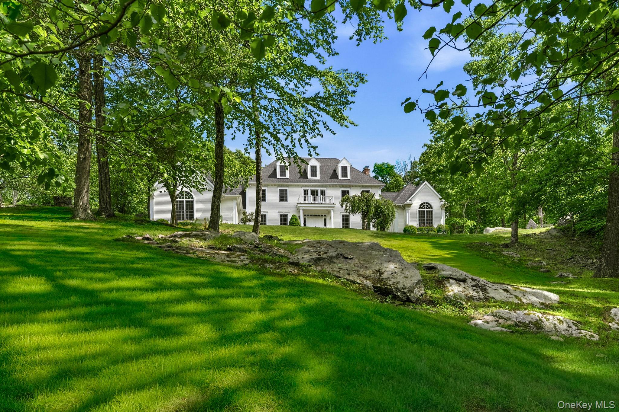 Elegant and timeless, this five-bedroom Georgian Colonial is set on a tranquil cul-de-sac, crowning a gentle rise amid sweeping meadows and striking rock outcroppings. Impeccably maintained, a two-story entry introduces interiors of classic elegance and finely crafted moldings, where gracious formal living and dining rooms unfold with ease.The magnificent music room showcases a cathedral ceiling and is flooded with natural light through oversized twelve-over-twelve windows. A sunken family room, anchored by a stately fireplace, opens through French doors to an inviting stone terrace - perfectly designed for both intimate moments and grand entertaining.A private first-floor bedroom suite with its own entrance offers exceptional flexibility for guests or extended stays. Dual staircases ascend to the upper level, where three well-appointed bedrooms accompany a serene primary suite featuring two walk-in closets, a fireplace, and a bath.An expansive bonus room offers endless possibilities for recreation, media, a home office, or additional accommodations. A spacious full basement with a walkout provides additional opportunities for recreation and versatile use. Outdoors, the grounds are graced with natural rock outcroppings and a generous level field, ideal for picnics or sports pursuits. Altogether, the property embodies a harmony of elegance, privacy, and refined living.