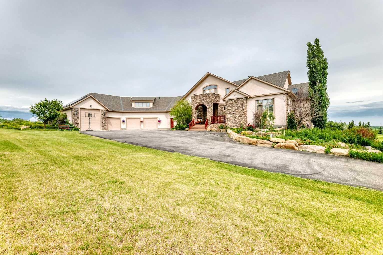 Perfectly positioned on prestigious Spruce Meadows Way, overlooking the world-renowned Spruce Meadows Equestrian Centre and directly across from Silverado, this exceptional 5.02-acre corner estate offers a rare combination of luxury, privacy, breathtaking 360° views, and future development potential. Located on Calgary's doorstep in one of the Foothills' most desirable locations, enjoy spectacular Rocky Mountain vistas, rolling countryside, and Calgary skyline sunsets.This custom-built executive residence offers over 6,300 sq. ft. of professionally developed living space (4,111 sq. ft. above grade plus 2,224 sq. ft. walk-out), showcasing exceptional craftsmanship throughout. Rich custom cherry woodwork highlights the home, while the chef's kitchen features handcrafted cherry cabinetry, premium built-in appliances, a large island with cooktop, prep sink, built-in desk, display cabinetry, and a separate spice kitchen.The stunning two-storey Great Room features a dramatic curved wall of floor-to-ceiling windows framing panoramic views, complemented by a one-of-a-kind handcrafted sculpted ceiling. The main floor includes a luxurious primary suite with a spa-inspired 5-piece ensuite and walk-in closet, a private library/den, and a second bedroom with its own ensuite.Upstairs, a bright loft opens to a sheltered south-facing balcony, while the spacious bonus room above the garage with a private ensuite is ideal as a guest suite, office, or additional bedroom.The fully developed walk-out level is designed for entertaining and family living, featuring a home theatre, spacious family room, custom wet bar, wine cellar, home gym, steam shower, two additional ensuite bedrooms, a flexible multipurpose room, and extensive storage with direct garage access.Additional highlights include a heated four-bay garage/shop with in-floor heating, RV-height fourth bay, 220V EV charging outlet, gated entrance, exterior entertainment speakers, and a comprehensive security system. Recent updates include new shingles (2021) and new eavestroughs and downspouts (2021).Designed as an ultra-energy-efficient Green Home, the property features a six-well geothermal heat pump system with natural gas backup, delivering exceptional comfort and low operating costs.Whether you're seeking a prestigious country estate, an exceptional equestrian property, or a strategic long-term investment with future development potential, this one-of-a-kind estate offers an unparalleled lifestyle just minutes from Calgary