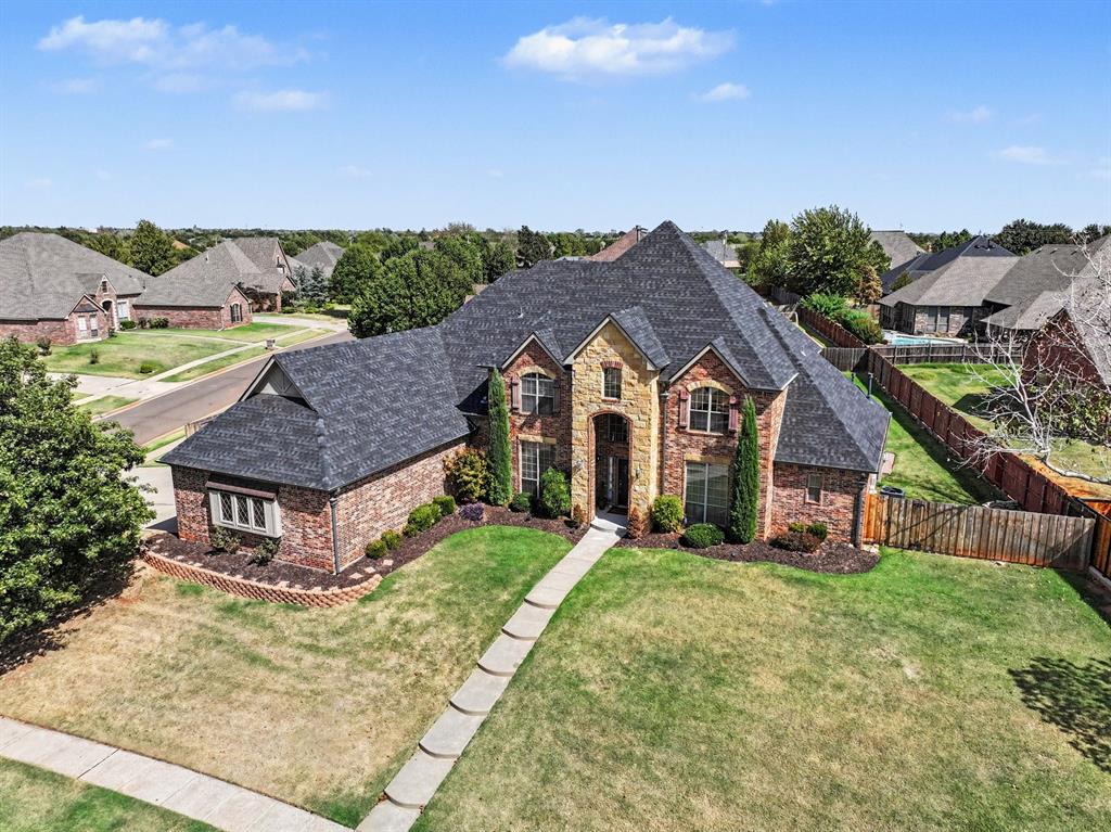 Set high on a beautiful half-acre corner lot, this exceptional brick-and-stone residence offers more than 5,300 square feet of living space with resort-style amenities. Soaring two-story ceilings and oversized windows create a welcoming atmosphere filled with natural light. The living room is anchored by a beautifully re-tiled fireplace and floor-to-ceiling windows overlooking the backyard. The expansive kitchen features granite countertops, double ovens, gas cooktop with custom brick surround, microwave drawer, pot-filler and oversized island with second prep sink. An oversized pantry provides exceptional storage. Kitchen and laundry room cabinetry have been professionally refinished and painted with soft-close doors and drawers and new hardware. The main-level primary suite offers direct access to the pool deck. The updated bath features a new quartz countertop, vessel sinks and faucets, new cabinet hardware, updated shower tile and new shower door, plus a walk-in closet. Also on the main level are a family room, formal dining room, breakfast room, laundry room, private office with French doors and guest suite with its own bath; offering a flexible multi-generational living opportunity. Upstairs, three additional bedrooms, one with an en suite full bathroom, an additional full bath, game room and dedicated theater room offer flexibility for guests and entertaining. Outside, the covered patio overlooks a heated in-ground pool with waterfalls, bubbler jets, tanning shelf and hot tub. An in-floor vacuum and cleaning system makes upkeep easy. Conveniently located near shopping, dining and everyday amenities with easy access to Edmond and Oklahoma City. With its generous corner-lot setting, unique architectural details, extensive living spaces, convenient location and resort-style backyard, this is a home designed to be enjoyed—not simply admired. This home is truly a rare opportunity to have the space, amenities and flexibility to accommodate the way you want to live.