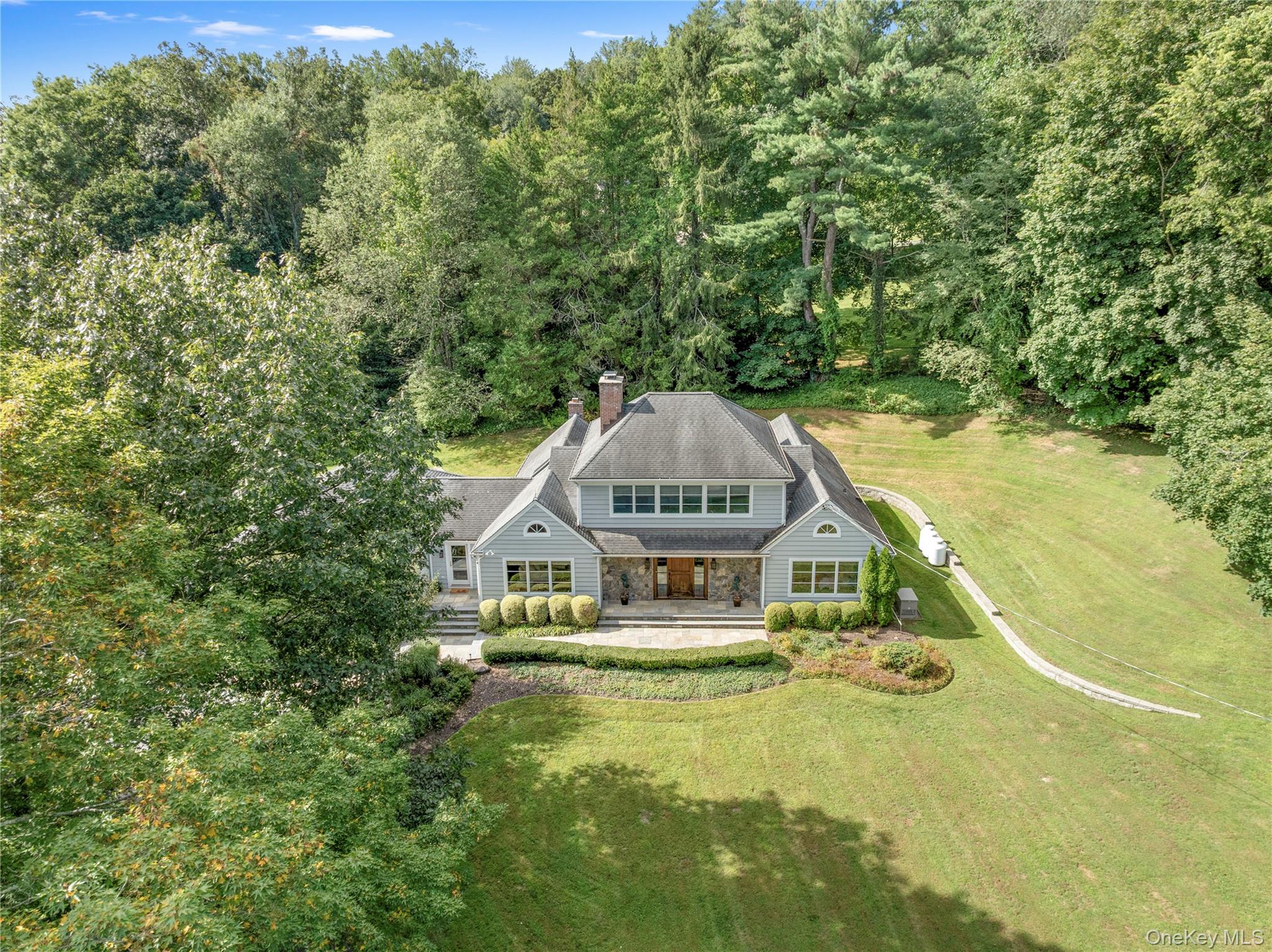 Welcome to 56 Annandale Drive, Chappaqua, a capacious and captivating Cape Cod commandingly set on 1.4 acres in sought-after Lawrence Farms East within walking distance to Mount Kisco Country Club, Kittle House, Chappaqua Crossing, Horace Greeley High School and the town of Mount Kisco. Built for entertaining, every day is a holiday to celebrate in the open, spacious interiors, starting with the inviting front-facing living room with wood-burning fireplace. The gourmet kitchen is equipped with solid wood cabinetry with pull-out shelving, tile backsplash, stone countertops, center island with prep sink, 5-burner cooktop, dual Thermador in-wall ovens, GE microwave, Sub-Zero refrigerator/freezer, and a Viking dishwasher. Host feasts or fests in the dramatic formal dining room with wood burning fireplace and opposing sets of French doors to opposing patios. BBQ on the built-in grill and dine alfresco on the patio. The party continues in the extra-spacious family room with large windows on three sides. Main-level private quarters include a front-facing in-law or guest suite with private, ensuite bath; and the king-sized primary suite endowed with its own sitting/dressing area, a sumptuous, private, resort-worthy ensuite bath, and French doors to the patio with swim spa for rejuvenation or relaxation. Completing the main-level are the entry foyer with two separate coat closets, broom closet and powder room; and a front-to-back mud room with front- and rear- facing French doors and garage access. Upstairs houses a wide, front-facing lounge or play space adjoining two rear-facing bedrooms with built-ins, outfitted, dormered closets with attic access, and sharing a “Jack-n-Jill” bath with double vanity, linen closet and tiled shower with in-wall jets and regular and handheld showerheads. Downstairs sit two generously sized recreation rooms; a full bath with shower; a laundry room equipped with Whirlpool front-loading washer and dryer, sink, ironing board and built-in cabinetry; storage; mechanicals; and access to the attached 3-car garage with electric car charger. An alarm system and a standby, backup, whole house generator help protect it all. A sweeping drive provides plenty of off-street parking. Lovely lawns and landscaping add colorful accents, and mature and established trees ring the perimeter of the property. A distinctive residence in a notable location.