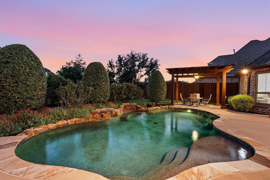 Welcome to this timeless elegant Country French-inspired Home by Oak Creek CUSTOM Homes in sought-after Griffin Parc! This one-owner, north-facing residence offers 5 bedrooms and 4.5 baths, 4,325 sq ft on an Oversized .270 acre, Green Belt Lot, with a Gold Medal Pool and 3-car garage. Freshly painted throughout, it features a dramatic 20-ft foyer, Juliet balcony, hand-scraped hardwoods, custom millwork, Private Study, formal dining room, and an inviting family room with natural light, views of the pool, and a stone-and-brick fireplace. The open kitchen offers custom cabinetry, stainless steel appliances, and updated quartz countertops with a marble backsplash. The spacious primary suite is a peaceful sanctuary with lush backyard views, direct patio access, a tray-coffered ceiling, crown molding, and in-ceiling speakers. The private first floor Ensuite Bedroom provides flexibility for guests or multigenerational living. Upstairs leads to 3 generously sized bedrooms, a Game Room, wet bar, study area, and Dedicated Theater with Panasonic projector, Definitive speakers, and a Stewart 120-inch screen complimented with scone lighting and detailed molding. Plantation shutters adorn all upstairs windows, while the bathroom vanities and wet bar have been refreshed with quartz countertops. Step outside to the spectacular Resort Style Backyard Oasis with pool, waterfalls, holes for a Volleyball net, covered patio and fireplace, two pergolas, built-in grill area, stone bar, and fire pit. Convenient to Top Rated FISD Schools (all within walking distance), two city parks within the neighborhood, highways, shopping, medical services, PGA attractions, and Universal Kids Resort. An Impact Resistant Shingled Roof was installed in 2023, and the 3 Trane HVAC units were replaced in 2021. A rare opportunity to enjoy timeless custom craftsmanship, versatile living spaces, thoughtful updates, and exceptional indoor-outdoor entertaining in one of Frisco’s sought-after communities.
