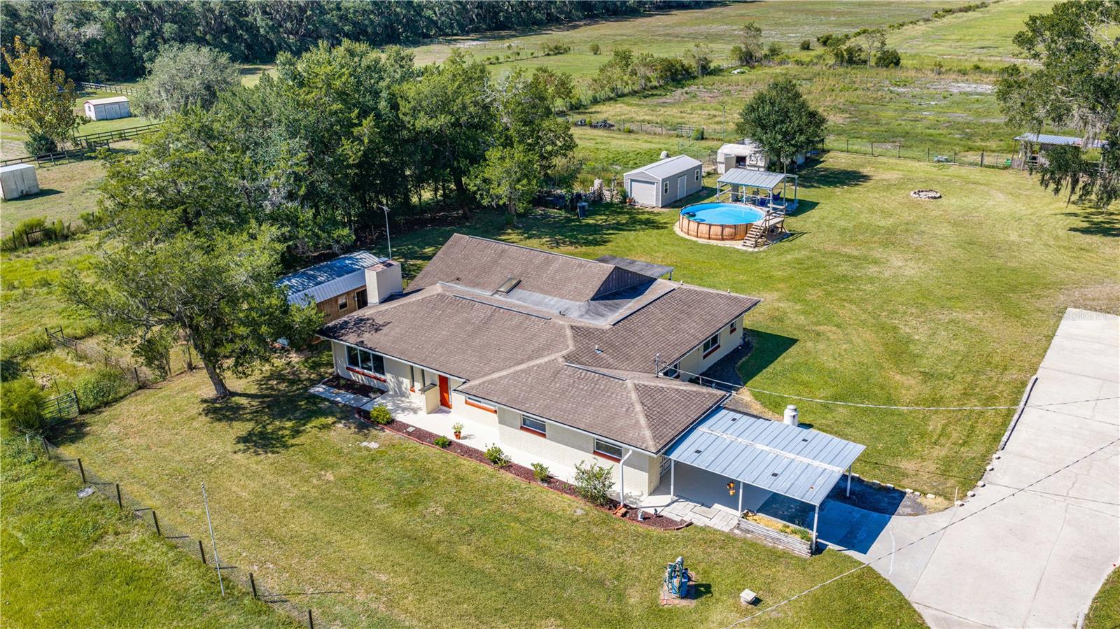 Enter through beautiful shade trees and a solar power operated gate, pass a picturesque pond and arrive at the main home on the left and secondary building on the right. A large driveway offers ample parking, while mature live oaks, fenced pastures and spectacular sunsets set the scene for country living.The updated main home offers 3 bedrooms, 3 baths, soaring ceilings, 2 spacious family rooms and a dining room. The kitchen is a baker's dream, with custom wood cabinetry by a local cabinetmaker, quartz countertops and an oversized island with abundant storage and outlets on both ends. A built-in baking nook hides behind cabinet doors, with power for your mixer and storage for supplies. Enjoy a Whirlpool gas range, stainless appliances, a pantry with a custom barn door and a sunny breakfast nook overlooking the pond.One family room features a brick fireplace, capped and fitted with an electric fireplace component. The dining room opens to a second oversized family room with vaulted ceilings and a beverage center with a bar fridge and wine fridge. Triple sliders lead to a covered patio with sunset views over the live oaks and pastures.Two generous en suite bedrooms have walk-in closets and updated baths. One bath features a custom vanity and step-in shower with bench, niche, grab bars and skylight; the other offers custom cabinetry and a jetted Jacuzzi tub. A third bedroom and updated full bathroom with a step-in shower complete the home. Additional updates include LED lighting, a 4-ton HVAC system installed in 2023, a 2023 Rheem hot water heater and replacement of most windows. The one-car garage houses the laundry.Across the driveway, the secondary building offers an updated 3-bedroom, 1-bath living space with its own kitchen and indoor laundry. The building was renovated, converted and permitted in 2019–2020, including a roof, windows, flooring, kitchen, bath, HVAC, water heater, electrical and plumbing. An attached oversized single-entry RV-sized garage and workshop has an approximately 10-foot-tall opening. Once fitted with a car lift, it retains flooring designed to accommodate one.Horse fencing with new posts installed in 2023 divides the property into pastures, growing areas, a citrus grove and spaces for animals. There's a 2-stall stable with storage, 3 smaller sheds and a large outbuilding. Chickens and turkeys live here now; the property has also accommodated goats and horses. Enjoy 4 newer citrus trees, a producing lemon tree, and apple, walnut and pecan trees. Water is distributed throughout the grounds for irrigation. Two freshwater wells include a primary well serving both living areas and a backup well, plus a Kinetico water softener and shared septic system and drainfield redone in 2019.Cool off in the above-ground pool, installed March 2026 with saltwater filtration, or relax on the covered patio at sunset. Whether you're dreaming of growing your own food, raising animals, creating the ultimate workshop or simply enjoying wide-open spaces, this versatile property offers an incredible opportunity to enjoy country living with the convenience of additional living space, extensive updates and room for all your hobbies!