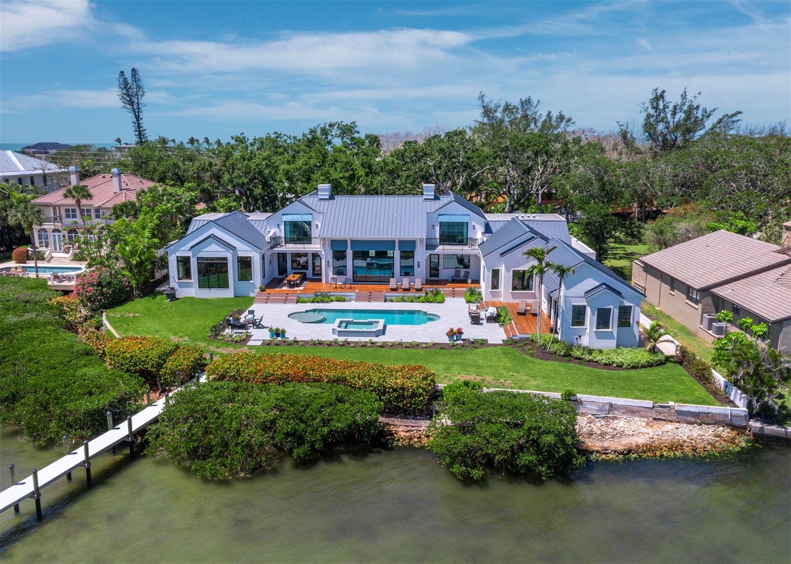 Welcome to one of the most impeccably reimagined residences at 8155 Midnight Pass on the quiet southern end of Siesta Key — a breathtaking bayside coastal estate that artfully blends modern innovation with timeless design. Set on nearly an acre of prime waterfront with 154 feet of shoreline, this gated property offers just under 7,500 square feet of luxurious living area with more than 9,200 total square feet of combined living and entertaining space, recently transformed through a full-scale two-year architectural renovation by Braidenview Architects and Christner Brothers — winners of the 2024 Aurora Grand Award for Best Renovated Home. From the moment you arrive at the gated motor court, you’ll be struck by the serenity of the grand live oaks, artistically designed landscaping, and elegant curb appeal. Inside, the home, with classical proportions, opens to soaring ceilings, DuChateau European oak flooring, and thoughtful details at every turn — from custom cabinetry and designer lighting to Euro-Wall sliders and state-of-the-art automation by Coastal Smart Homes. The heart of the home features multiple expansive living areas, all with views of Little Sarasota Bay and the Intracoastal Waterway from nearly every room, a show-stopping kitchen outfitted with Wolf and Sub-Zero appliances, double islands, and a butler’s pantry make for effortless entertaining. With four bedrooms, 2 of which offer additional sleeping areas in the suites, six baths, a private gym, a large office with two separate workspaces, a sewing/project room, and bespoke closets throughout — every space is both beautiful and functional. Step outside to enjoy a reimagined resort-style pool and new spa, Brazilian IPE decking, and multiple areas to savor sunsets over the Intracoastal Waterway. For boating enthusiasts, there is an impressive 200-foot dock with lift to accommodate a 25’ vessel plus an additional mooring area. Whether hosting a family celebration or simply savoring the coastal breeze, this property is designed for making lasting memories. Plus you are minutes from Siesta Key beach when you want to take a walk and put your toes in the famed quartz-sand as you watch the sun disappear into the horizon. With Sarasota’s vibrant cultural offerings, shopping and dining just moments away, you are all set to enjoy every imaginable amenity for an impressive lifestyle.