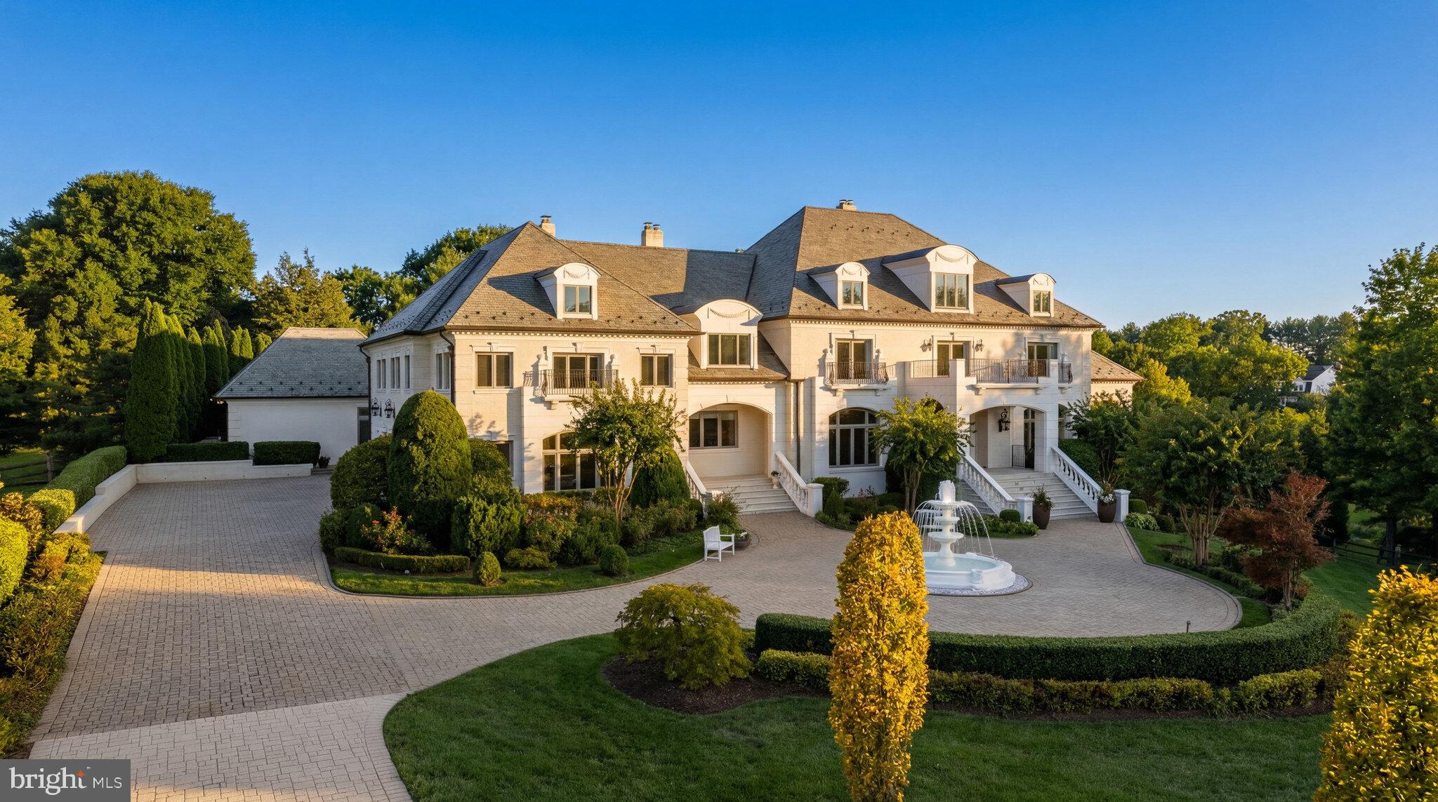 Set on a bucolic two-acre estate behind wrought iron gates along one of Vienna’s most distinguished corridors, 1521 Hunter Mill Road is a residence of uncommon scale, craftsmanship, and sophistication. A long paver driveway framed by manicured landscaping creates a formidable approach to the central motor court revolving around an elaborate fountain. Classic architectural symmetry, a slate roof, expansive terraces, and a resort-caliber outdoor environment establish a sense of arrival and permanence. A residence exuding grandeur and recently enhanced with thoughtful modern upgrades, the estate offers more than 15,000 square feet of luxury across the main residence and pool house, each space designed to elevate daily living and lavish entertaining.Inside, a soaring two-story grand foyer lined with gleaming inlaid marble floors beneath a shimmering crystal chandelier introduces a generously proportioned floor plan. The space flows effortlessly ahead into the dramatic two-story great room crowned by an 18-foot cathedral ceiling. Formal spaces include richly appointed embassy sized living and dining rooms, as well as a dignified library, balanced by casual gathering areas. Natural light floods through UV-tinted windows along the rear elevation, framing views of the terraces and grounds while protecting interiors from the elements.At the heart of the home lies a chef’s kitchen. Fully reimagined in 2023, the transitional space is both functional and aesthetically cutting edge, appointed with quartz countertops, top-of-the-line Wolf appliances, a butler’s pantry, and a walk-in pantry, all adjoining a two-story breakfast room overlooking the pool terrace. The main-level primary suite is a private refuge, featuring a serene sitting room, dual walk-in closets, and a spa-inspired marble bath. Upstairs, five additional bedroom suites, each with its own full bath, including a private guest suite or tucked away office, offer exceptional comfort. A private guest suite on the uppermost level further enhances multigenerational flexibility or telecommuting capacity.Not so much an entertainer’s delight as it is an independent destination, the lower level’s roster of resort-like amenities includes a professional home cinema, multiple recreation and game rooms, billiards room, fitness center, and sauna. The level also features walk-out access to the backyard, allowing indoor leisure spaces to flow seamlessly into the estate’s outdoor environment. A full suite with private bath, extensive storage and utility rooms, and dedicated media and equipment spaces ensure the level is both functional and indulgent. Complementary culinary spaces on the lower level include a catering kitchen, wet bar, and a kitchenette in the in-law suite, completing the estate’s ethos of comprehensive hospitality.Modern systems seamlessly support the property’s scale. Multiple newer HVAC units, a Lutron smart lighting system, and upgraded infrastructure provide convenience, efficiency, and peace of mind. A three-car garage, supplemented by an additional single-bay garage, completes the offering.Out back, an expansive elevated stone terrace overlooks an immense manicured, level rear lawn with unbroken sightlines, granting a sensation of seclusion within a close-in location. At the center is a large heated lap pool and accompanying semicircular hot tub. An outdoor kitchen pavilion extends the living experience outdoors, creating a sanctuary for al fresco dining. An enclosed pool house is self sufficient, showcasing its own kitchenette and living space that can fully open onto the terrace to blur the lines between indoor and outdoor living.1521 Hunter Mill Road is a rare opportunity as an estate which blends grand architectural scale with modern livability, luxurious amenities, and a resort-like outdoor environment — all within minutes of the vibrant heart of Vienna, Tysons, and the Capital Region — for a truly unparalleled lifestyle.