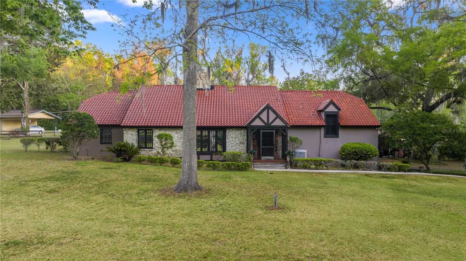 PERFECT FOR MULTI-GENERATIONAL FAMILIES OR INCOME PRODUCING! Nestled on 1.45 acres, these two timeless French Country style homes exude old-world European charm with rustic elements and understated elegance. The main home offers 3 bedrooms, plus office, 3.5 baths, and a dramatic tri level design, with a striking stone fireplace serving as the focal point of the grand living area. Rich oak hardwood floors, a parquet entry, plantation shutters, and knotty pine shelving and closets add warmth and character throughout. The spacious primary suite includes a sitting room overlooking the aviary, while the first floor features a quaint chef’s kitchen with Saltillo tiled floors and stainless-steel appliances, seamlessly connecting to the cozy family room and glass-enclosed lanai. This space leads to the inviting 16 x 36 pool and courtyard, where the sweet scent of jasmine fills the air. The charming Carriage House is a versatile addition, offering 1 bedroom, 2 full bathrooms (first floor wheel-chair accessible), a full kitchen, and an office—perfect for extended family or as an income property. The property is beautifully landscaped, with serene water fountains, statues, and a park-like setting that creates a tranquil sanctuary. Additional amenities include 2-car garage, tennis court, carport with an attached storage shed, a play area with swings and climbing bars, and an elegant steel gate, adding the perfect touch of sophistication to this extraordinary estate.  Short distance to downtown Ocala, restaurants, major hospitals, Florida Horse Park, World Equestrian Center and more! Don't wait and make your appointment today!