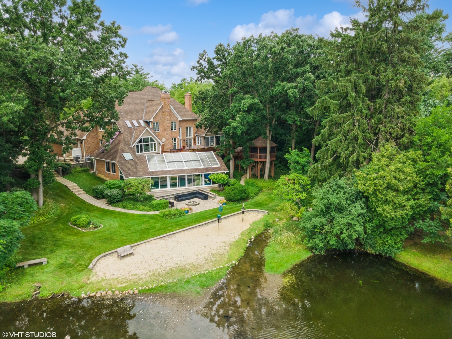 An extraordinary retreat on Bishop's Lake in Kildeer, this 5.5-acre estate blends rugged nature with sophisticated luxury. Just minutes from downtown yet worlds away in serenity, it offers sweeping lake views, mature trees, and a private resort lifestyle.  Inside, the home stuns with a grand stairwell accented by a 20-foot stone waterfall, custom millwork throughout, and four fireplaces that create warmth and character in every season. The dramatic great room features soaring ceilings and walls of glass that frame ever-changing lake vistas and flood the space with natural light. At its center is a true highlight-an extraordinary $300K walnut kitchen, showcased on HGTV's "I Want That." Recently enhanced with new quartz counters and top-tier stainless appliances, it blends striking design with everyday functionality.  Resort-style amenities extend beyond the walls: a treehouse-style gazebo, private beach with lake access for swimming and kayaking, and a year-round indoor pool with a waterfall that feels like a world-class spa. Wildlife is part of the daily rhythm here-swans gliding across the water, deer along the treeline, egrets soaring overhead, and excellent fishing right from your shoreline.  Whether entertaining by the lake, enjoying quiet mornings on the beach, or relaxing fireside after a swim, this estate delivers a rare balance of natural beauty and sophisticated design in one of Kildeer's most coveted settings.
