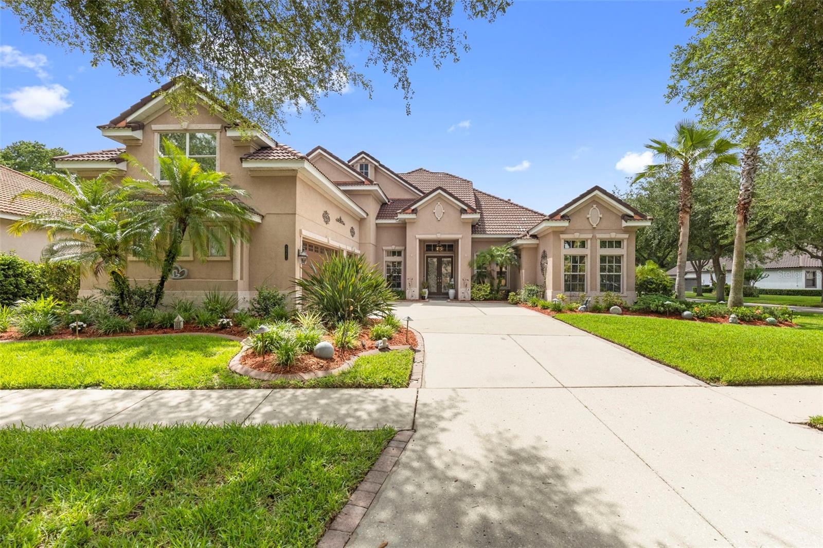 Virtually Staged. Positioned on a premium corner lot within the highly sought after gated community of Grand Hampton, this exceptional 5 bedroom, 5 bathroom pool home offers 3,947 square feet of thoughtfully designed living space, luxury upgrades, and timeless elegance. Florida friendly landscaping, landscape lighting, a paver driveway, architectural detailing, and stunning stained glass entry doors create unforgettable curb appeal.Inside, soaring ceilings, abundant natural light, and an updated crystal chandelier make a striking first impression. The formal dining room, highlighted by its own crystal chandelier, flows seamlessly into the living room with French doors opening to the lanai.Designed for entertaining and everyday living, the chef's kitchen features 42 inch cabinetry, updated hardware, under cabinet lighting, an updated backsplash, granite countertops, a newer sink and faucet, LG appliances, and a spacious eat in area. The kitchen overlooks the family room and offers direct outdoor access.The first floor primary suite is a private retreat featuring tray ceilings with crown molding, lanai access, dual California closets, and a spacious ensuite with dual vanities, Corian countertops, a glass enclosed shower with dual shower heads, a jetted soaking tub, and a spacious flex space.Also on the main level are three additional bedrooms, including a secondary bedroom with engineered hardwood flooring, a custom California closet, and access to a full pool bath. Two additional bedrooms with California closets and updated carpet share a Jack and Jill bath with an updated tub enclosure. A laundry room with cabinetry, utility sink, oversized storage closet, and adjacent built in desk area complete the first floor.Upstairs, the fifth bedroom features hardwood flooring, a California closet, and a private ensuite bath with an updated tub enclosure. A custom library with glass shelving and extensive storage, a large loft featuring hardwood flooring, and an additional full bathroom provide exceptional flexibility. The loft opens to a private balcony finished with low maintenance Trex decking.The outdoor living space is a true private oasis. Enjoy a screened lanai with a resurfaced heated pool and spa, covered entertaining areas, a gazebo, mature landscaping, and a fenced pool equipment enclosure. The pool and spa were resurfaced in 2020. The pool heater and pump were replaced in 2024.The oversized 3 car garage features epoxy flooring, storage shelving, metal tool cabinets, a built in workbench, and upgraded lighting.Additional updates include a tankless gas water heater (2023), interior repainting, 3M window film, a hardwood staircase, and a washer, dryer, range, and refrigerator replaced in 2022.Grand Hampton residents enjoy a 24 hour manned gate, resort style clubhouse, 24 hour fitness center, a lagoon pool with water slide, lap pool, tennis courts, basketball courts, parks, lake access, and multiple gazebos. Conveniently located near I 75, I 275, AdventHealth, PHSC, AdventHealth Center Ice, The Shops at Wiregrass, and Tampa Premium Outlets.