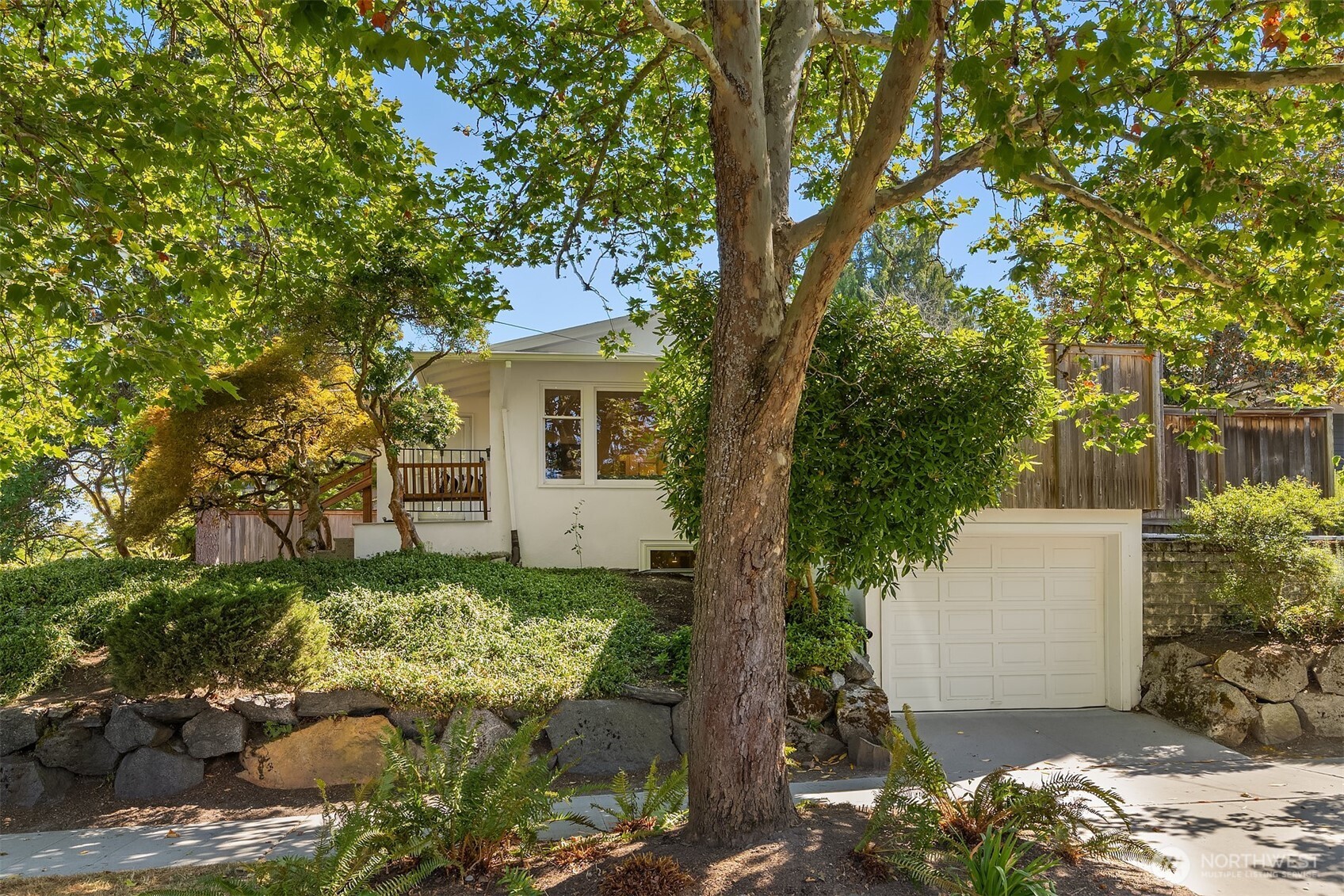 Classic 1925 Mission-style Craftsman pairs exceptional character with extensive modern updates in desirable Ravenna. Elevated corner lot creates privacy, while arched passageways, hardwood floors, coved ceilings, custom built-ins + dramatic wood-burning fireplace make an unforgettable first impression. Vintage-inspired kitchen features white cabinetry, distinctive tilework + newer stainless appliances. Two main-level bedrooms + remodeled full bath. Full lower-level renovation adds approx. 500 SF with private third bedroom, flexible second living area, remodeled 3/4 bath with heated floor + dedicated laundry. Enjoy a private deck off dining room, fenced yard + attached garage with EV charger. Updated plumbing, electrical + panel, earthquake retrofit, mini-split heat/AC + drainage improvements. Near Ravenna Park, UW, shops, dining + light rail.