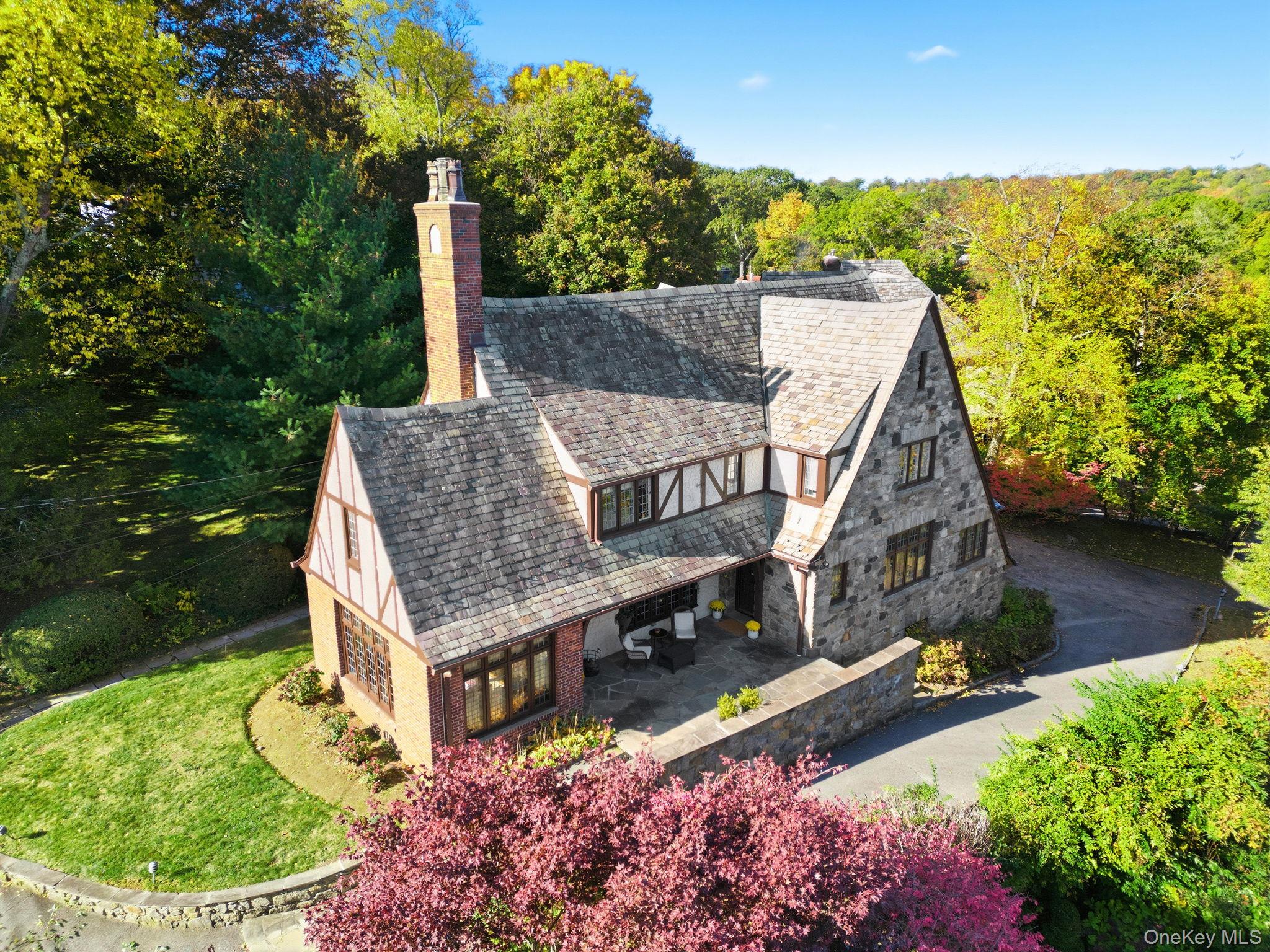 Grand 1925 Tudor showcasing timeless architectural elegance with a gracefully graduated slate roof, a striking blend of stone and brick, and subtle wooden accents. Nestled on half an acre in the highly sought-after Edgemont School District, this home is within walking distance to the Jr./Sr. High School, Scarsdale Golf Club, Hartsdale train station, and a vibrant array of dining options. Step inside to experience the home’s historic charm, enhanced by an abundance of leaded and stained glass windows that bathe the interiors in natural light, complemented by gleaming hardwood floors throughout. The airy living room features a hand-carved stone fireplace mantel, while the grand foyer boasts a bespoke oak staircase. The renovated eat-in kitchen is both stylish and functional, paired with a formal dining room and an inspirational sunroom, currently used as an office. Ascending the staircase, crowned by a breathtaking floor-to-ceiling stained glass window, you’ll find a spacious primary suite complete with a full bathroom and dressing room, along with three additional bedrooms and a hallway bathroom. The basement offers a versatile recreational space ideal for a gym, laundry room, and convenient access to the large attached 2-car garage. This home is a true masterpiece, blending classic grandeur with modern comforts in an unbeatable location!