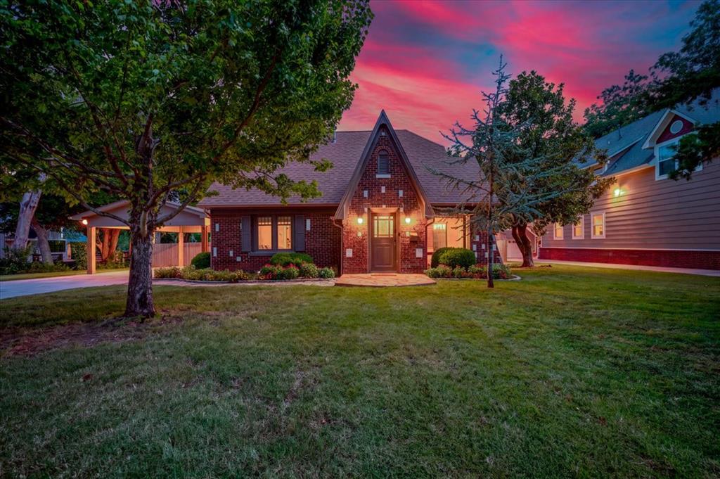 Most homes this close to campus sit on a quarter acre or less. This one sits on a fully fenced 0.91 unplatted acre in the Southridge area, just blocks to OU, Memorial Stadium, The Mont, and Campus Corner. The large lawn stretches from the house back to a canopy of mature shade trees. This 1930 Tudor has the steep gables, leaded glass, and brick detail that lovers of vintage homes look for, and a thoughtful renovation has preserved all of it. The original woodwork has been sanded, stained, and sealed, the hardwood floors refinished, the bathrooms fully renovated, and all new lighting added throughout. The kitchen offers new stone countertops, a commercial size gas range, double wall ovens, and peninsula seating, as well as a family dining area. Outside, the renovation continues with all new cedar privacy fence, new carport, new concrete patio, and manicured landscaping. Copper gutters and an electric vehicle charger at the carport round out the exterior. Mornings start with coffee on the front screened porch, with its arched brick openings and imported tile. Evenings settle in with a good book by the brick fireplace. Game weekends move to the covered deck and patio, overlooking your expansive lawn with plenty of room for your own long pass. Five bedrooms include an upstairs retreat with French doors to a balcony over the yard, ideal as a study or guest suite. Whether this becomes your primary home, a game day home, or a weekend retreat, it offers something rare: it's close enough to campus to be part of everything core Norman and University life offers, with enough land to step out back to your private retreat.
