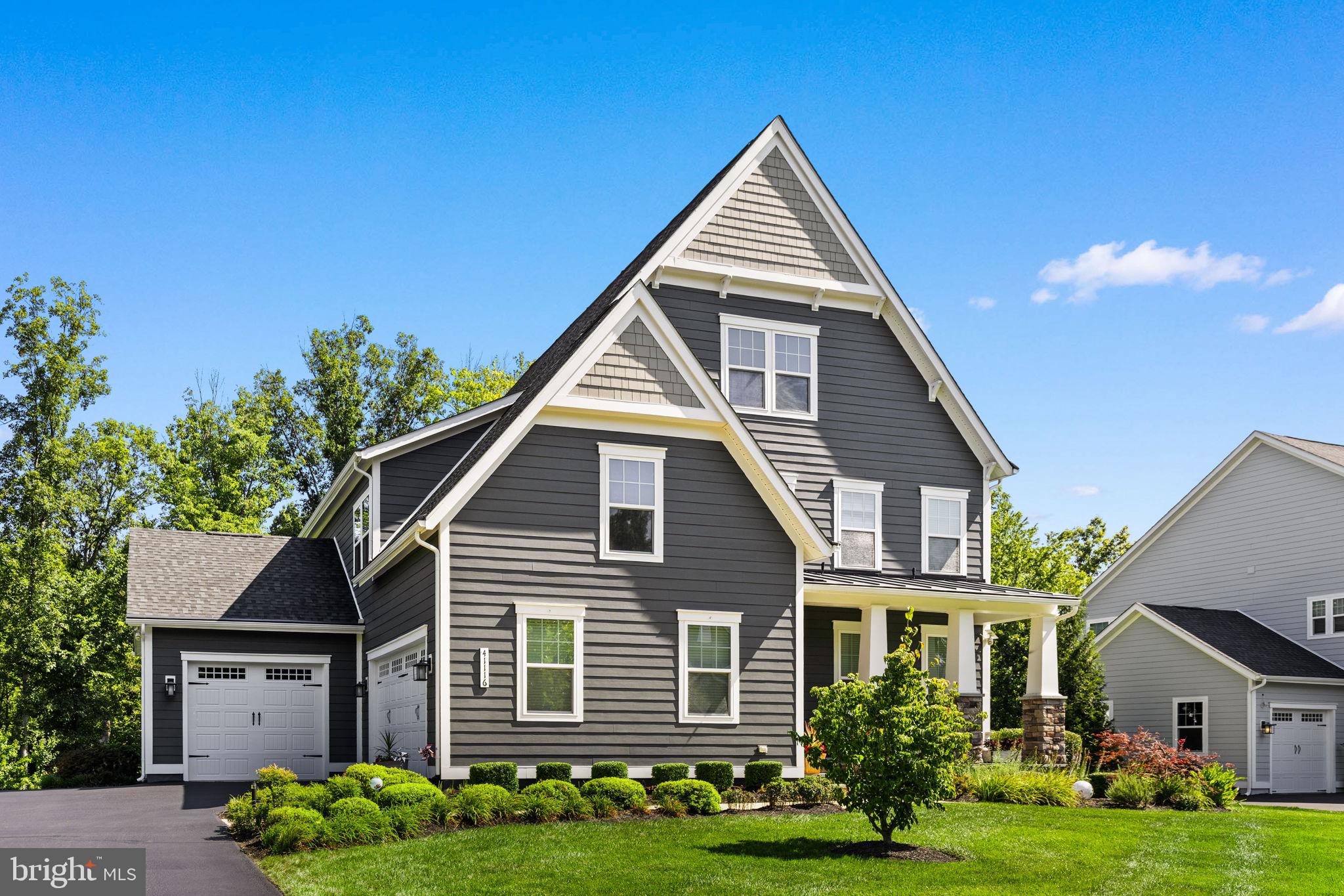 Nestled on a premium lot beside open green space and backing to mature trees, this exceptional 2018 Danville model offers beautiful curb appeal and an outstanding sense of privacy from the moment you arrive. The stone-accented front porch provides the perfect place to relax while taking in the peaceful surroundings. Inside, nearly 4,700 square feet of thoughtfully designed living space blends generous proportions with everyday comfort. Rich dark hardwood floors extend from the welcoming foyer into a private home office featuring a custom sliding barn door. Just down the hall, a flexible room currently serves as a sun-filled art studio, highlighting the versatility of the floor plan. The heart of the home is the expansive gourmet kitchen, stretching over 21 feet, complete with crisp white cabinetry, a farmhouse sink, double wall ovens, and an oversized granite island. The kitchen flows seamlessly into the spacious dining area and 17 x 17  family room, where a custom wood-plank accent wall creates a warm and inviting gathering space. Nearby, a custom mudroom with built-in cubbies and bench seating adds both style and functionality. Outdoor living is equally inviting. Oversized windows and a glass door fill the home with natural light while leading to a generous composite deck. Below, a beautifully designed paver patio features a built-in fire pit and under-deck string lighting. Backing to a tranquil canopy of mature trees, the backyard offers exceptional privacy for entertaining or quiet evenings outdoors. Upstairs, an oversized laundry room adds everyday convenience. Each secondary bedroom offers generous space and large closets, while the expansive primary suite spans more than 19 feet and features dual walk-in closets and a spa-like bath with a soaking tub. The fully finished walk-out lower level expands the home's living space with a 38-foot recreation room featuring continuous hard-surface flooring. A custom tasting bar with dual wine refrigerators creates the perfect setting for entertaining, while a fifth bedroom and full bath provide comfortable accommodations for guests. A dedicated exercise room with some equipment conveying  completes the lower level. Rounding out this exceptional home is a rare split three-car garage and an outstanding location within the highly sought-after Greens Village of Willowsford, where scenic open space, resort-style amenities, and an exceptional lifestyle come together to create one of Loudoun County's most sought-after communities.