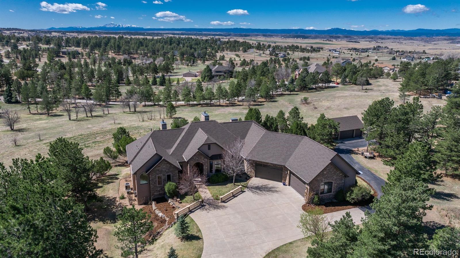 Set on five private, tree filled acres in the sought-after Sterling Tree Farm community, this striking 7,000-square-foot custom home blends modern style with timeless luxury, all framed by unobstructed Pikes Peak views. Thoughtfully designed as an ideal family home, it offers abundant space both inside and out, with plenty of room to live, gather, and play. The main level has been refreshed with updated, contemporary paint tones, creating a clean, elevated aesthetic that complements the rich mahogany detailing throughout. Designed with today’s lifestyle in mind, the layout offers generous, flexible spaces that allow families to spread out comfortably while still feeling connected. A chef-inspired kitchen with a Butler’s pantry anchors the space, while the formal dining room makes a statement. Two expansive main floor bedrooms each feature their own private laundry, offering comfort and convenience with a thoughtful, modern touch. Architectural highlights include a stunning main-level library that adds character and craftsmanship you don’t often find. The lower level is designed for both entertaining and everyday living, with 3 additional bedrooms, a second laundry room, a high end theater, and a beautifully finished secondary kitchen.  A handicap-accessible basement entrance further enhances functionality and ease of access. Outdoor living is equally inviting, with a serene water feature, private patio, and three expansive decks perfectly positioned to take in the mountain views. There’s ample room for outdoor fun, including dedicated spaces to play and a classic horseshoe pit, perfect for gathering with family and friends. The property also includes an oversized four-car attached garage and a 1,800-square-foot outbuilding with a 3-car garage door ideal for storage, hobbies, or a workshop. Private, polished, and perfectly located near Parker, this home delivers space, style, and sophistication.