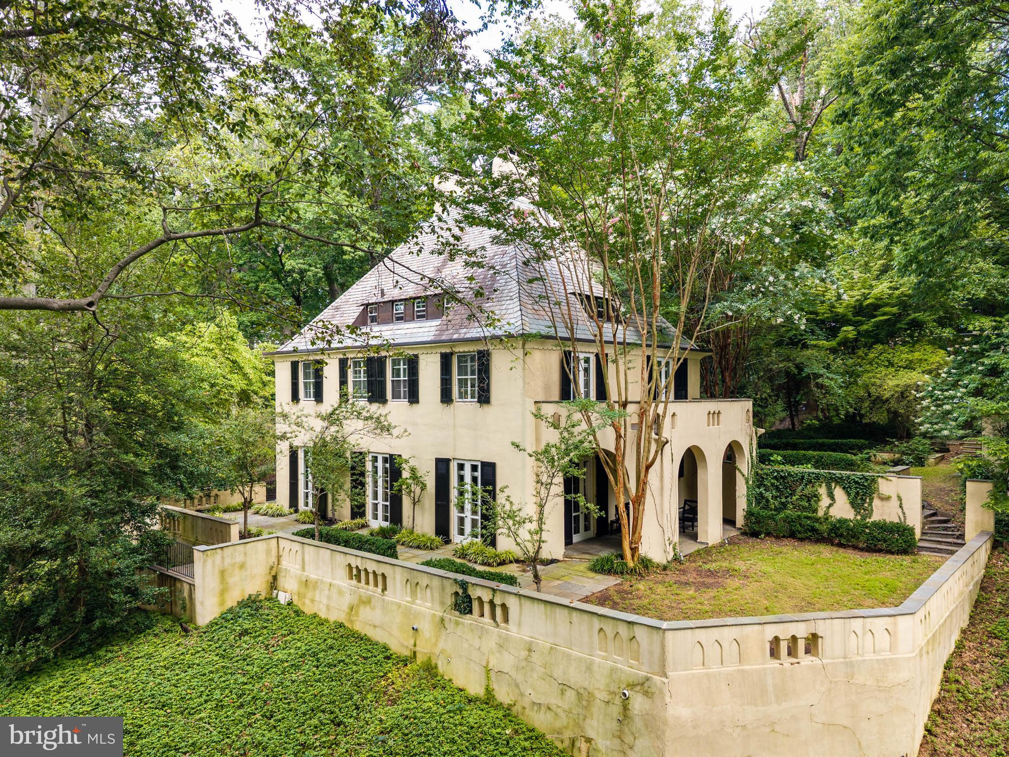 Privately set on just over an acre in the heart of Wynnewood, 100 Cherry Lane is a captivating 1925 residence distinguished by its romantic European-inspired architecture, exceptional privacy, and enduring Main Line character.The home is rich in architectural detail from the moment you enter. A handsome foyer introduces substantial millwork, built-in bookcases, a fireplace, and a staircase accented with distinctive Mercer tile. Arched openings, exposed beams, French doors, deep window openings, and multiple fireplaces continue throughout, giving the interiors warmth, texture, and a sense of authenticity rarely found in newer construction.The principal rooms are gracious and beautifully proportioned. The living room and dining room offer inviting spaces for both everyday living and entertaining, while French doors open to terraces and garden areas that extend the home outdoors. A richly detailed library with extensive built-ins provides an ideal office, reading room, or intimate retreat.The kitchen combines character with function, featuring a large center island, granite countertops, professional-style range, Sub-Zero refrigeration, generous cabinetry, and an adjoining breakfast area. Its scale and configuration make it equally suited to casual meals and larger gatherings.Upstairs, the primary suite is especially appealing, with a fireplace, French doors to a private terrace, and an en-suite bath. Additional bedrooms and baths are arranged across the upper levels, creating flexibility for family, guests, offices, or other uses.The exterior spaces are among the home’s most memorable features. Covered arched loggias, broad stone terraces, garden walls, and mature landscaping create a series of private outdoor rooms for dining, entertaining, or quiet enjoyment. The terraces offer captivating views across the lush, tree-canopied setting, creating a remarkable sense of privacy and connection to nature.A two-car attached garage, finished lower-level space, central air, and ample off-street parking add everyday practicality.Located in the Lower Merion School District, 100 Cherry Lane is just minutes from Suburban Square, the train to Center City, Wynnewood and Ardmore shopping and dining, and all major transportation routes. It is a rare combination of architectural charm, privacy, character, and convenience in one of the Main Line’s most desirable locations.