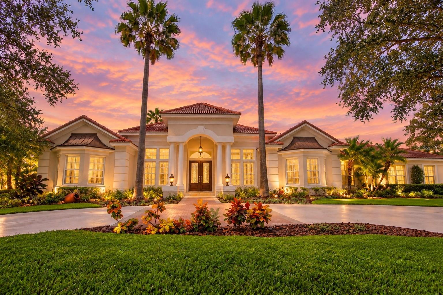 An extraordinary setting, custom architecture, and one of New Tampa’s most impressive water views. Custom built by Flair Homes on an expansive waterfront homesite, this residence offers sweeping views and exceptional privacy.From the moment you arrive, the home makes a statement. A circular driveway, side-entry garage and mature landscaping introduce a residence filled with timeless architectural detail. Step inside to soaring ceilings, graceful archways, extensive crown molding, decorative niches, detailed ceiling treatments and abundant natural light. The main living areas have been enhanced with high-quality imported Turkish marble flooring, adding richness and continuity throughout.The formal living room is exceptionally elegant with an intricate custom ceiling design, crystal lighting and French doors framing views of the pool and water beyond. The separate formal dining room continues the sophisticated architectural detailing and provides an impressive setting for entertaining. A private home office features soaring ceilings, custom built-in display niches, plantation shutters and abundant natural light.At the heart of the home is an expansive, fully remodeled kitchen that is every bit as impressive as the setting. Rich custom cabinetry extends nearly to the ceiling and is accented by illuminated glass-front display cabinets and generous storage. Granite countertops provide abundant workspace, complemented by a large center island and oversized breakfast bar. The kitchen features stainless steel appliances, double wall ovens, a sleek cooktop, pot filler, under-cabinet lighting and detailed tile backsplash. Multiple windows and the adjoining casual dining area offer beautiful views of the pool and waterfront.Open to the kitchen, the spacious family room offers a warm and inviting contrast to the home's more formal spaces. A fireplace serves as a focal point beneath a dramatic ceiling, while a wall of windows fills the room with light and brings the outdoors in.The outdoor living space may be the home's greatest luxury. A large covered lanai and expansive brick-paver pool deck surround the custom swimming pool and spa, offering exceptional space for dining, relaxing and entertaining. Beyond the screen enclosure, the oversized homesite opens to a broad lawn, mature palms and spectacular views across the pond toward the country club. The setting is private, peaceful and distinctly Florida.Located within the 24-hour manned gated community of Hunter’s Green, residents enjoy parks, tennis and basketball courts, athletic fields, playgrounds, a dog park and walking paths. Conveniently located near I-75, USF, Moffitt Cancer Center, shopping, dining and entertainment at The Shops at Wiregrass and Tampa Premium Outlets.