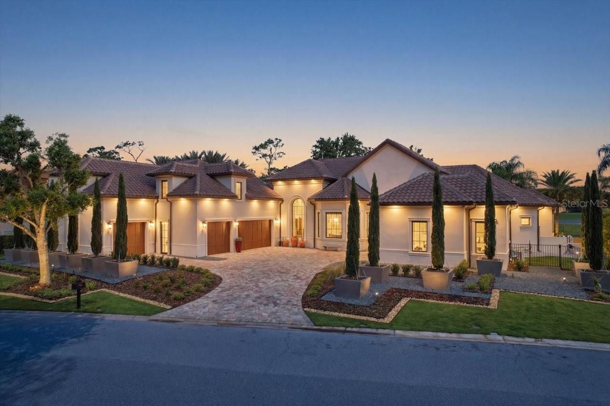 Overlooking the 7th hole of Lake Nona Golf & Country Club, 9599 Blandford Road presents a reimagined single-story residence defined by sweeping golf and water views, elevated privacy, and a seamless connection between indoor and outdoor living. Completed through a DeVoe remodel, the home reflects a refined balance of architectural intention and modern livability, curated for both elevated entertaining and effortless daily living.A thoughtfully reimagined arrival introduces the home with presence. The redesigned driveway and expanded garage enhance both scale and functionality, offering generous parking and flexibility. Newly installed pavers are framed by pristine landscaping and twelve anchored potted trees, creating a clean, architectural approach.Positioned to fully capture its golf and water frontage, the outdoor living spaces unfold as a natural extension of the home. The backyard features refreshed landscaping, a resort-style pool and spa, a fully equipped summer kitchen, and a sculptural pergola crafted from imported Canadian lumber, an environment suited for both quiet mornings and entertaining.Inside, a redesigned entry reveals a light-filled interior defined by volume, proportion, and uninterrupted sightlines through to the pool and fairway beyond. Dekton flooring anchors the main living areas, while curated lighting, including a statement chandelier, adds a refined, modern layer. The kitchen serves as both an architectural feature and gathering space, with quartz surfaces, dual sinks, double ovens, an induction cooktop, wine refrigeration, an instant hot faucet, and integrated pull-out pantry storage. A built-in breakfast nook introduces a more relaxed setting, while cove lighting enhances the ceiling architecture and overall spatial experience.The adjacent living area is elevated by Walker Zanger “Matouche” crocodile flooring in the dining room, offering a setting that transitions effortlessly between relaxed evenings and entertaining at scale. Each of the four bedrooms is designed as a private retreat, all with en-suite bathrooms, including a secondary bath serving the pool. Bathrooms feature quartz surfaces, refined fixtures, and modern tile selections.The primary suite offers scale and privacy, complemented by a renovated bath and a custom-designed closet with extensive built-ins, a 15-drawer island, and a dedicated luggage closet. A private office overlooks a tranquil pond and preserve, complete with roller shades and custom built-ins.The expanded garage includes additional storage, a dedicated workshop, and its own AC. Above, a fully air-conditioned space with private exterior access offers flexibility as a guest suite, fitness studio, or retreat. The laundry room functions as a mudroom with built-in storage.Set within one of Central Florida’s most sought-after private communities, residents enjoy access to Lake Nona Golf & Country Club amenities, including dining, tennis, fitness, social events, and a driving range just moments away—completing a lifestyle defined by privacy, design, and ease.