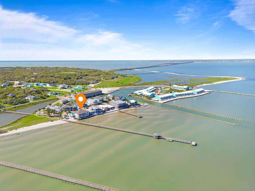 Tucked behind the gates of Sea Shell Shores, lies a home of uncommon design & turn-key waterfront living on a private sandy beach in a one-of-a-kind setting for a grand coastal living experience. This bayfront sanctuary wasn't just renovated, it was reimagined to embrace its surroundings & life on the water. Right outside, the bay awaits. Reel in a huge redfish, launch your boat, or simply sit at the water's edge. There's more. The property extends its exclusivity with a 1/4 acre lot in the adjacent Bahamas subdivision, granting access to the private lighted pier, residents-only beach & boardwalk. Inside, the home unfolds with purpose. Walls of windows frame ever-changing views of Aransas Bay. Open-concept design flows with ease, from a sun-soaked living area to a culinary space where conversation gathers around quartz counters, custom cabinetry & a wine & whiskey parlor for a quiet indulgence or a lively toast. The primary suite is perched above the bay, where morning light spills across the room & an electric fireplace sets the tone for restful nights. The en-suite spa, wrapped in marble with a stand-alone soaking tub feels more like a spa than a bathroom. Downstairs, games continue in the entertainment lounge, a 2nd kitchen & private guest suite with infrared sauna & beverage station. Another guest suite with family-ready accommodations, queen bed & built-in bunks. Step outside, towering palms sway above a newly landscaped yard. Stone steps lead to the private beach where you can play or lounge at the water's edge. A 65-jet spa & cozy seating areas offer the perfect place to soak in the sun or share quiet time at dusk. Every element was chosen to make life effortless and secure—newly installed bulkhead and a 60-foot dock, advanced 2023 HVAC system, home generator, handcrafted railing system & smart lighting. Sold with majority of furnishings. A place where every day feels like the beginning of something special. Here, nature is an integral part of the lifestyle.