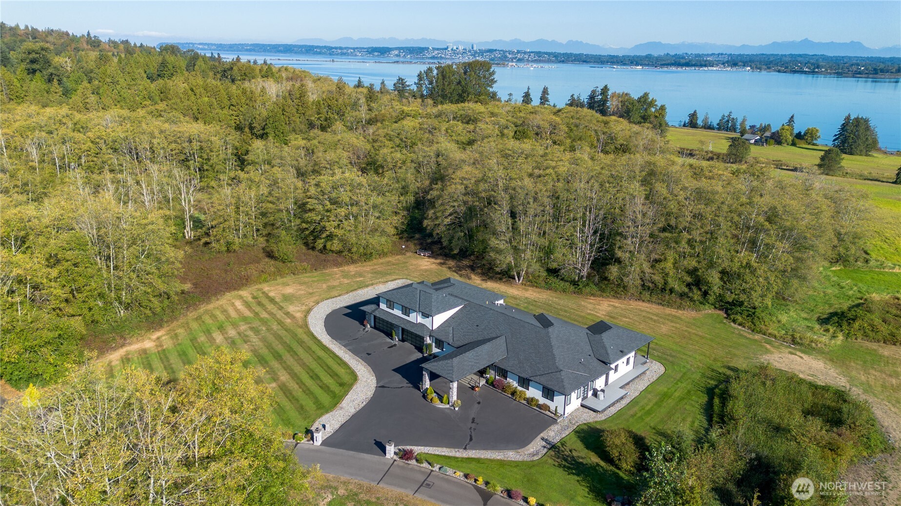Some homes impress with their finishes. This one earns admiration for everything behind the walls. Set on 5.82 private acres in the gated Heronswood community, this extraordinary custom estate pairs a beautiful water view of Drayton Harbor with views of majestic Mt. Baker. Located at the end of a quiet lane, it is one of only 13 homes surrounded by approximately 48 acres of preserved open space, creating an exceptional sense of privacy. Every detail reflects a commitment to craftsmanship, comfort, and longevity—from radiant heated floors, soaring 13-foot ceilings, and expansive walls of glass to a true chef’s kitchen designed for serious cooking and entertaining. The primary suite is thoughtfully secluded from the gathering spaces, while every guest bedroom features its own ensuite bath. An expansive deck extends the living outdoors and takes full advantage of the beautiful setting. Nearly 3,000 square feet of garage & workshop space provides room for vehicles, hobbies, projects, and storage, while nearly 1,000 square feet of unfinished bonus space with plumbing and electrical already in place offers remarkable flexibility. Behind the scenes, commercial-grade mechanical systems, whole-home water purification, extensive sound insulation, and carefully engineered infrastructure elevate this home beyond custom construction. Minutes from Semiahmoo Resort, championship golf, beaches, marina, and the Canadian border, this is Pacific Northwest estate living at an exceptional level.