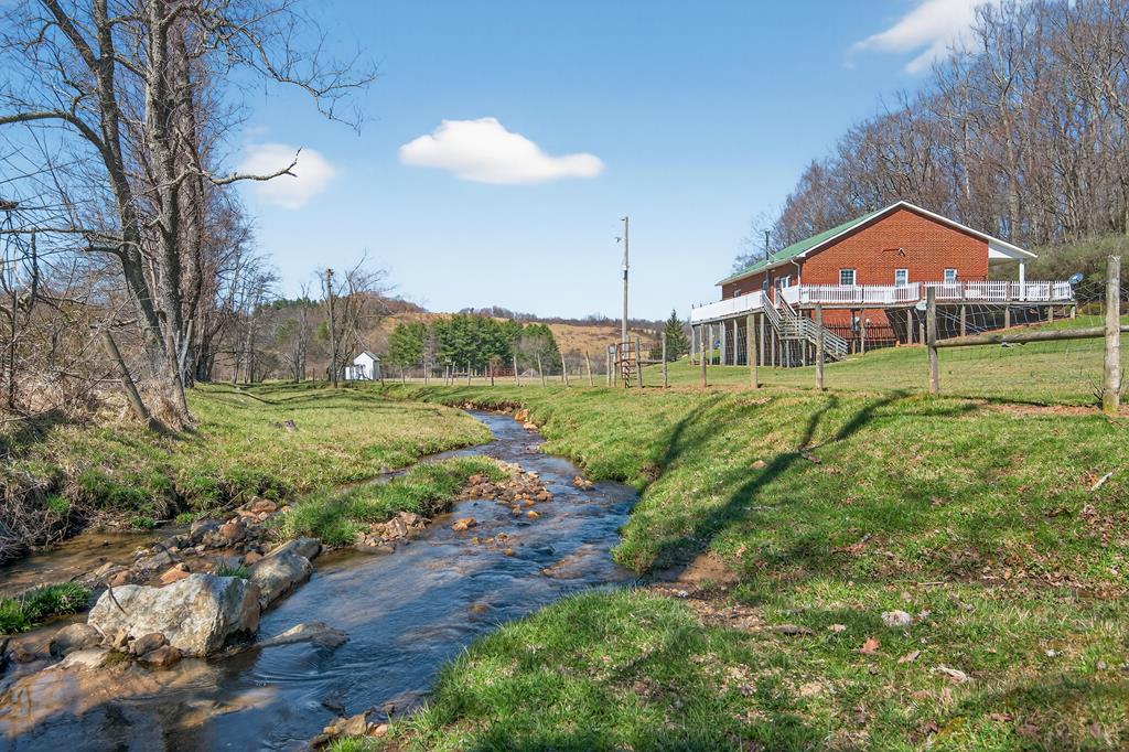 Here's your Peaceful Mini Farm Retreat with Creek and Mountain Views near Hillsville! Discover the perfect blend of privacy, productivity, and panoramic beauty on this fully fenced 11.75 acre mini farm featuring over 1,200 feet of flowing creek frontage! Ideally located just outside of Hillsville, only one mile from the Blue Ridge Parkway, minutes to I-77, and approximately one hour to Winston-Salem, this rare mountain property offers endless possibilities. The well-maintained, 1,750 sq. ft. brick home features 3 bedrooms and 2 full baths with calming countryside views from the open-concept living, dining, and kitchen areas. The spacious living room showcases hardwood flooring, while the dining area and kitchen offer ceramic tile, solid oak cabinetry, major appliances, and a stainless steel backsplash. The primary suite includes a walk-in closet and private full bath, there are two additional bedrooms, a full hall bath, and a welcoming foyer leading to the covered front porch and side deck to complete the main level. A full-length back deck provides the perfect setting to relax and take in the peaceful scenery. Downstairs, the full basement boasts 10-foot ceilings for easy finishing, a pellet stove and wood stove, commercial shelving, and sliding doors that open to a concrete patio overlooking the creek and rear acreage. Additional features include, main-level laundry, heat pump, sheetrock behind the paneling, metal roof, an attached garage, powered workshop for equipment storage, a children's playhouse with lean-to, a dog lot, and 24 x 40 pole barn! There's also a fenced-in homesite on the property with water and septic ready for hookup! Whether you envision farming, multi-generational living, investment income, or simply enjoying the tranquil sound of the creek in a scenic mountain setting, this property delivers exceptional opportunity and value. Here's your chance to experience life in the Blue Ridge, call today to schedule an appointment to take a look!