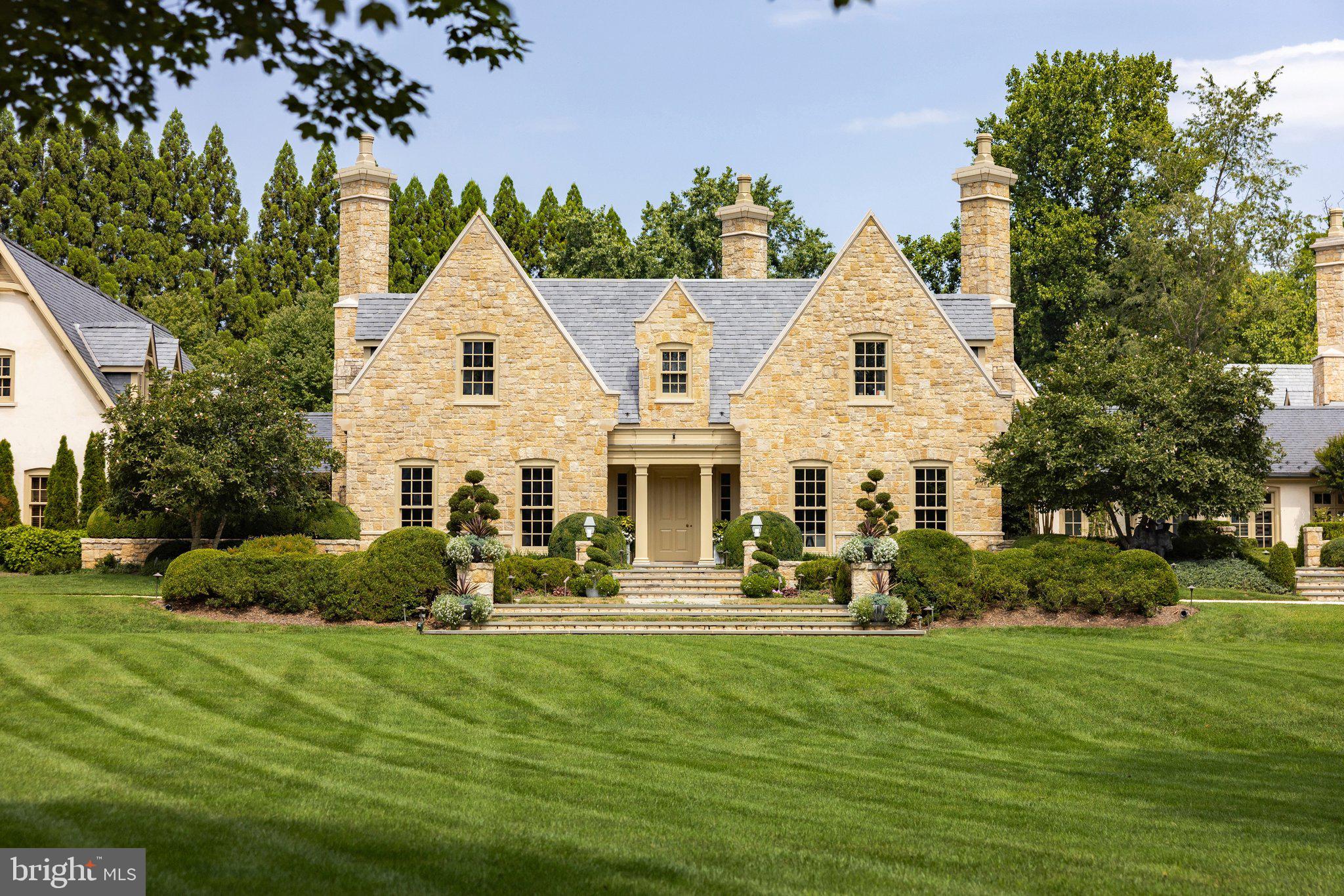 Set among the rolling hills of Great Falls, Alderley Manor is an estate on five acres, inspired by European traditions. The grounds evoke the English Cotswolds, where light-stone manors rise above open expanses and long vistas.The residence was a collaboration between David Cooper of ACG Architects and BOWA Construction, with further enhancements by Hanlon Design Build. Spanning more than 20,000 square feet, the estate showcases exceptional craftsmanship, timeless style, and premier amenities. A pea stone driveway leads to a central flagstone motor court, where imported Cotswold limestone, a slate roof with metal seams, copper gutters, and freshly repainted woodwork set a tone of enduring grandeur. Classic symmetry, steep gables, and towering chimneys create a striking first impression, balanced by warmth. Every exterior window and door is framed in rich mahogany, underscoring the commitment to quality and authenticity.Inside, reclaimed antique oak floors and hand-finished millwork reflect the same meticulous standards. Formal and informal rooms are proportioned to feel both expansive and inviting. Exquisite moldings, hand-carved details, custom built-ins, and oversized fireplace mantels with marble hearths enrich the interiors. The layout maintains symmetry while allowing a natural, intuitive flow. Top-tier finishes and fixtures support both grand-scale entertaining and daily living.The main level features elegant formal rooms, including a moody library with deep green built-ins and bold ceiling wallpaper, and a light-filled main gallery connecting the east and west wings. Informal spaces center around the chef’s kitchen with twin islands, furniture-grade cabinetry, a Lacanche range, and artisanal tilework. The adjacent breakfast room, with exposed beams, a stone accent wall, and multiple French doors, opens to the grounds. The west wing is dedicated to the primary suite, with a private garden, sitting room, dual dressing wings, and two luxurious baths. Two offices, including one with a vaulted beamed ceiling, complete the level.Upstairs, four bedrooms each showcase a unique design sensibility and are served by Lagos Azul limestone baths with Waterworks fixtures. The lower level is designed for leisure and entertaining, with a transverse gallery leading to a professional cinema, climate-controlled wine cellar, and a fitness center with spa bath, steam shower, and cold plunge, plus billiards and art studio spaces. Behind the scenes, commercial-grade systems ensure seamless living, including a self-sustaining well and septic, whole-house generator, Lutron lighting, smart HVAC, and a comprehensive security system.Outdoors, the gardens are extraordinary. With an investment exceeding eight figures, the landscaping and horticulture reach a world-class standard, creating a tapestry of manicured gardens, mature trees, and seasonal blooms. The setting is fully irrigated and softly illuminated by custom landscape lighting with hundreds of concealed fixtures that bring the property to life after dark. A heated lap pool with a retractable cover, a pergola-covered dining terrace, and a newly installed sports court provide exceptional opportunities for recreation and relaxation. For the automotive enthusiast, a modern farmhouse-style garage offers three bays, two lifts, a mezzanine lounge, and a cigar bar.While secluded, Alderley Manor is less than a mile from Great Falls Village and minutes from Tysons Corner, the Reston Tech Corridor, and Washington, D.C.With its rare combination of space, craftsmanship, architectural integrity, and refined amenities, Alderley Manor ranks among the region’s most exceptional private estates.