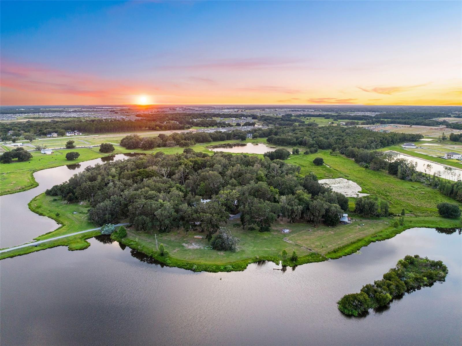 Offered for the first time in more than half a century, Magnolia Island Estate is one of Central Florida's last great private legacy estates. Nestled within one of Florida's fastest-growing communities, this breathtaking 95 - acre private wildlife sanctuary is where nature, history, and unparalleled privacy exist in perfect harmony. Hidden behind a private gated entrance in the heart of Wesley Chapel, a long drive leads to a secluded island surrounded by shimmering waters. Throughout the day, the estate comes alive with Sandhill Cranes, Roseate Spoonbills, Wood Storks, Great Blue Herons, bald eagles, deer, wild turkeys, and countless other native species, creating an authentic Old Florida experience rarely found today. Thoughtfully positioned on the property, the nearly 4,700-square-foot residence (7,584 square feet under roof) offers timeless craftsmanship, expansive windows, and breathtaking views from nearly every room. Designed for both comfortable family living and grand entertaining, the home features 5 bedrooms, 4.5 bathrooms, vaulted ceilings, a dramatic great room with a wood-burning fireplace, and an open-concept kitchen and dining area that serves as the heart of the home. The primary suite is privately located on the main level and features two walk-in closets. Also on the first floor are a dedicated home office, a private guest suite with its own walk-in closet and separate entrance, plus a spacious game and workout room just off the kitchen. Upstairs, three additional bedrooms and two full baths provide comfortable accommodations for family and guests. Just beyond the living spaces, the screen enclosed pool provides the perfect setting to relax, entertain, and enjoy Florida's sunshine year-round while taking in the peaceful sights and sounds of the surrounding landscape. Perhaps no space captures the essence of Magnolia Island more than the expansive wraparound porch. Enjoy peaceful mornings with coffee, spectacular sunset views reflected across the water, and evenings beneath star-filled skies while watching nature unfold before you. The cypress sided barn reflects the enduring character of Old Florida ranch heritage, offering two stalls along with ample space for hay, equipment, and tack storage. Whether envisioned as an equestrian facility, collector's barn, workshop, or gathering space for family events, it offers endless possibilities. Further enhancing the estate's setting, directly across the street the Southwest Florida Water Management District has acquired 938 acres that will become a nature park. Having nearly 1,000 acres protected across the street is something very few luxury properties can offer! Adding to the property's exceptional location, it is directly across from the Kirkland Ranch Academy of Innovation, a state-of-the-art public school recognized for its STEM focused curriculum, technology integrated learning, and innovative career. After more than fifty years of thoughtful stewardship, Magnolia Island Estate represents far more than an extraordinary residence. It is not simply a place to live, it is a place to preserve, a place to gather, and a place where future generations will write the next chapter of an extraordinary legacy.