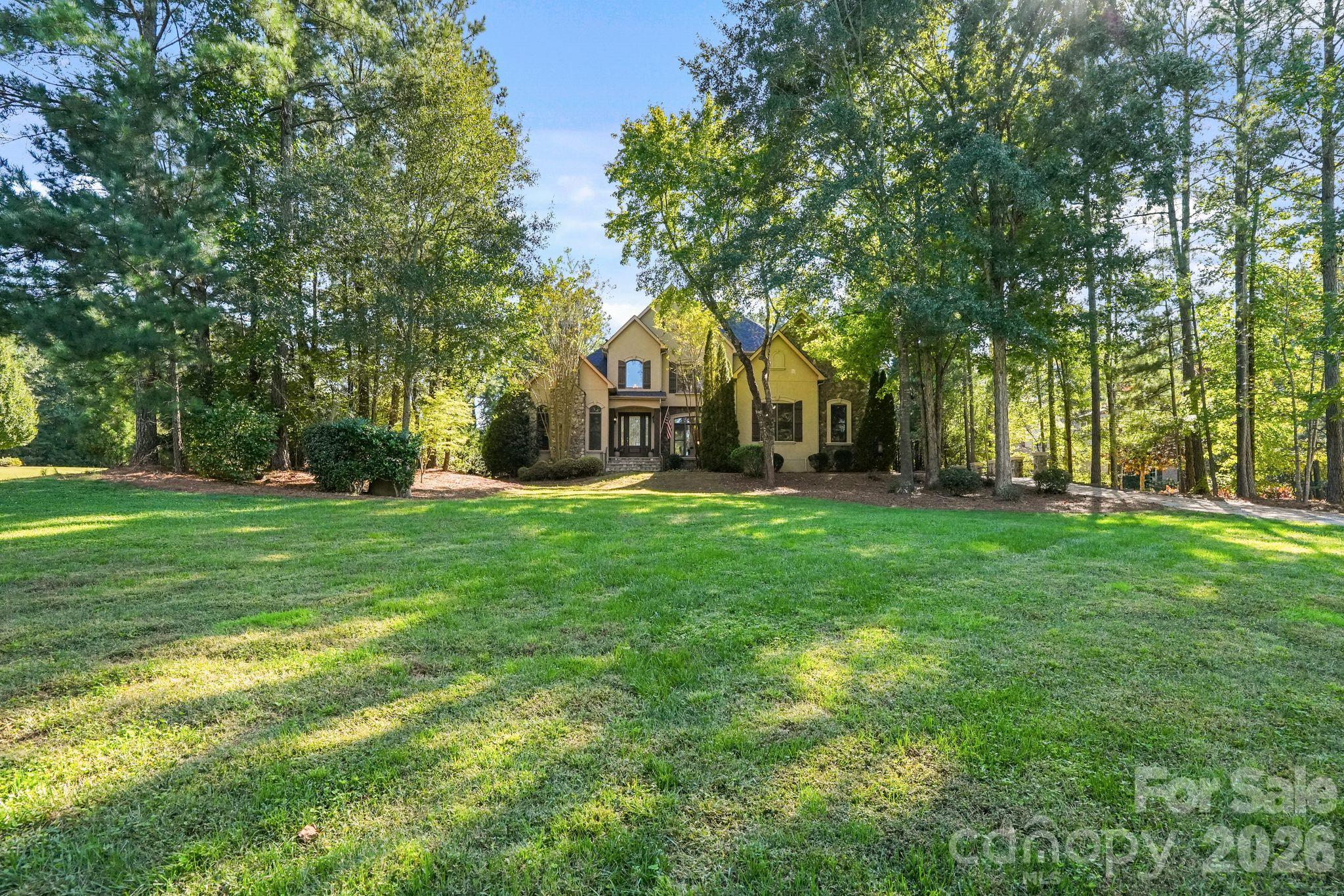 Located in sought after Trinity Ridge, a Fort Mill community known for its acre plus lots, mature hardwood trees and natural setting, this custom home sits on 1.45 beautifully landscaped acres. It's rare to find a backyard that offers this much, with a heated pool and spa, waterfall fountain, stone patio with outdoor fireplace, huge screened porch with gas log fireplace and an expansive, fenced lawn. Equally impressive inside, the two story great room is filled with natural light from its large windows. A double sided fireplace serves as a focal point between the great room and the kitchen/breakfast area, which opens to an adjoining morning room. Together, these spaces create an open, natural flow. Overlooking the great room, the upstairs catwalk with hardwood floors and wrought iron spindles adds to the home's open, airy feel. The main level includes a spacious primary suite and a richly paneled office, both with their own fireplaces. Hardwood floors, detailed moldings, coffered ceilings and custom trim add character throughout. Upstairs offers three additional bedrooms, including one with a private ensuite bath, a bonus room and an oversized unfinished storage room with easy access and plenty of space to keep everything organized. Additional highlights include a three car garage, York County only taxes and Fort Mill schools, including Catawba Ridge HS. Just minutes from the new Harris Teeter anchored shopping center under development, bringing additional restaurants, shops and everyday conveniences to the area.