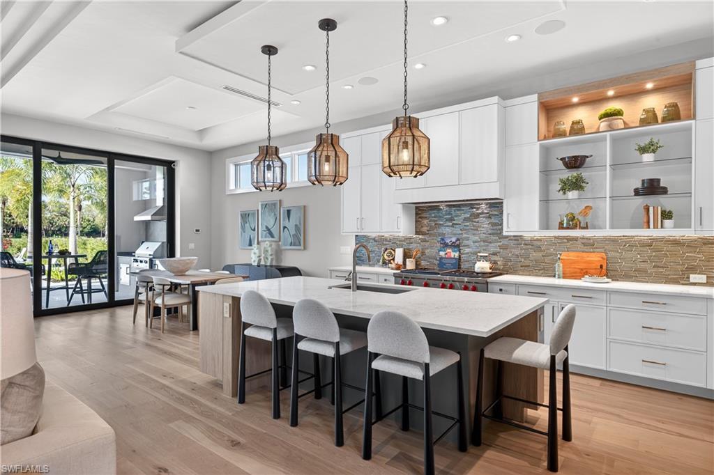Kitchen with a kitchen island with sink, light stone countertops, a kitchen breakfast bar, decorative light fixtures, and light wood-type flooring