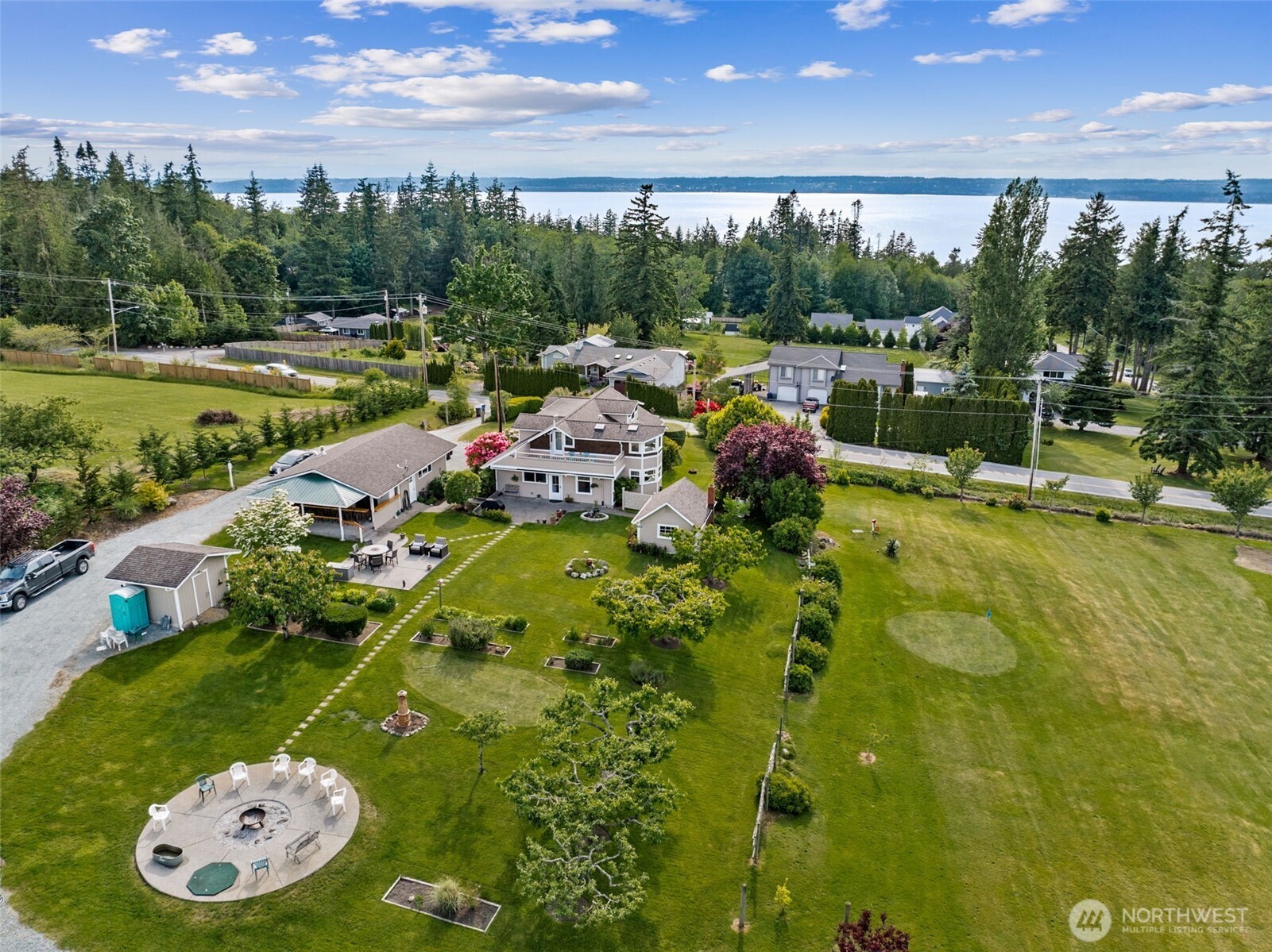 Entertainer & Golfer’s Paradise! Private 5-acre estate w/ 9-hole par-3 course—sand traps, pro signage & cart incl. Flexible acreage ideal for events, hobbies, animals or future ADU. Main home features wood floors, propane FP, kitchen w/ hickory cabs, tile counters, pantry & water view. Showstopping bar w/ cherry cabs, granite, mosaic tile & martini-glass ceiling. Lofted primary suite w/ 2 view decks—sunsets over Port Susan & sunrises over the course—plus spa bath. Guest house, bsmnt suite, huge heated shop w/ 220, tall doors & wkshp. Outdoor bar, patios, gardens, fruit trees & more!
