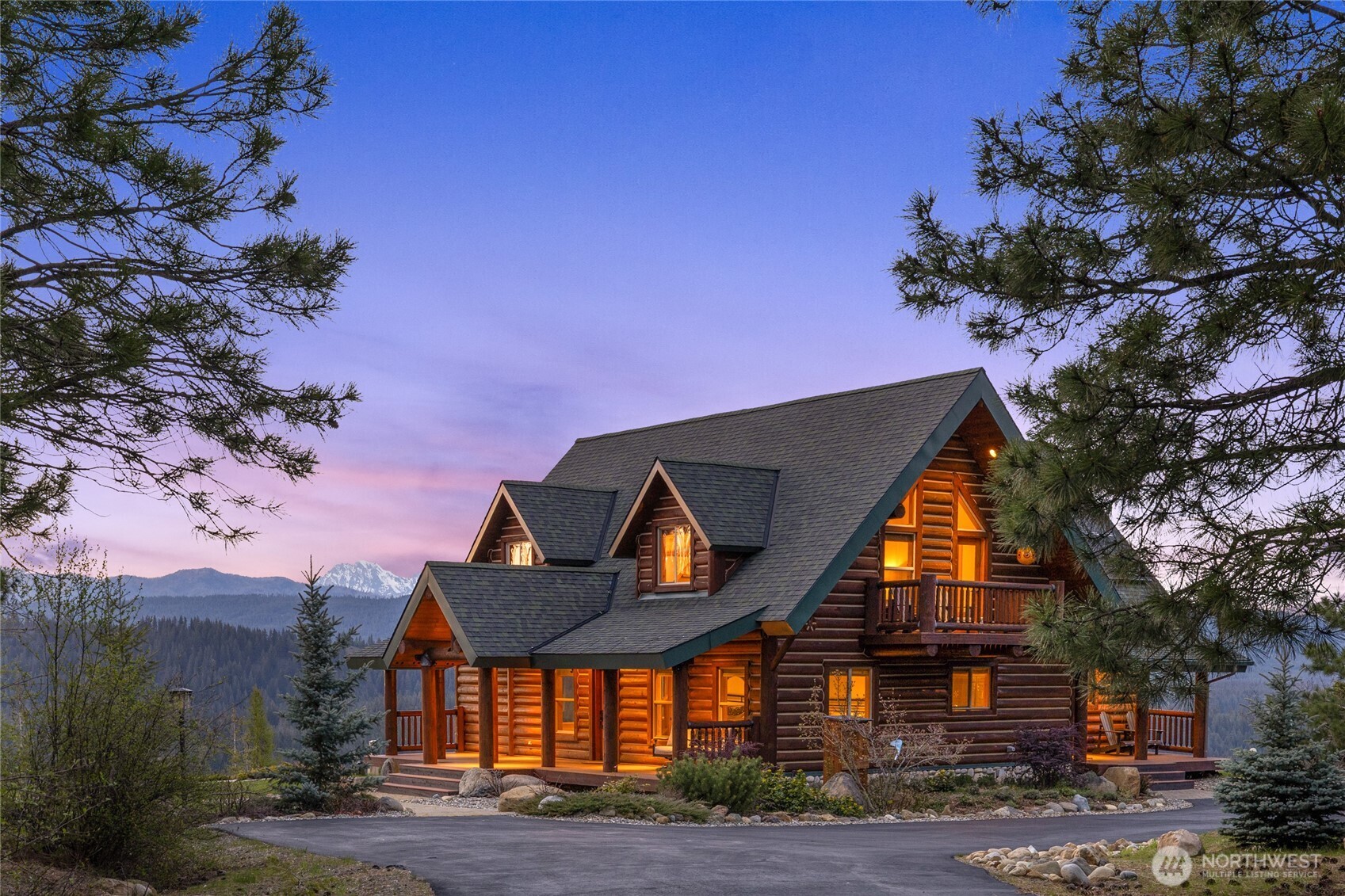 Twilight view highlighting the home’s covered porches, log construction, and surrounding mountain landscape.