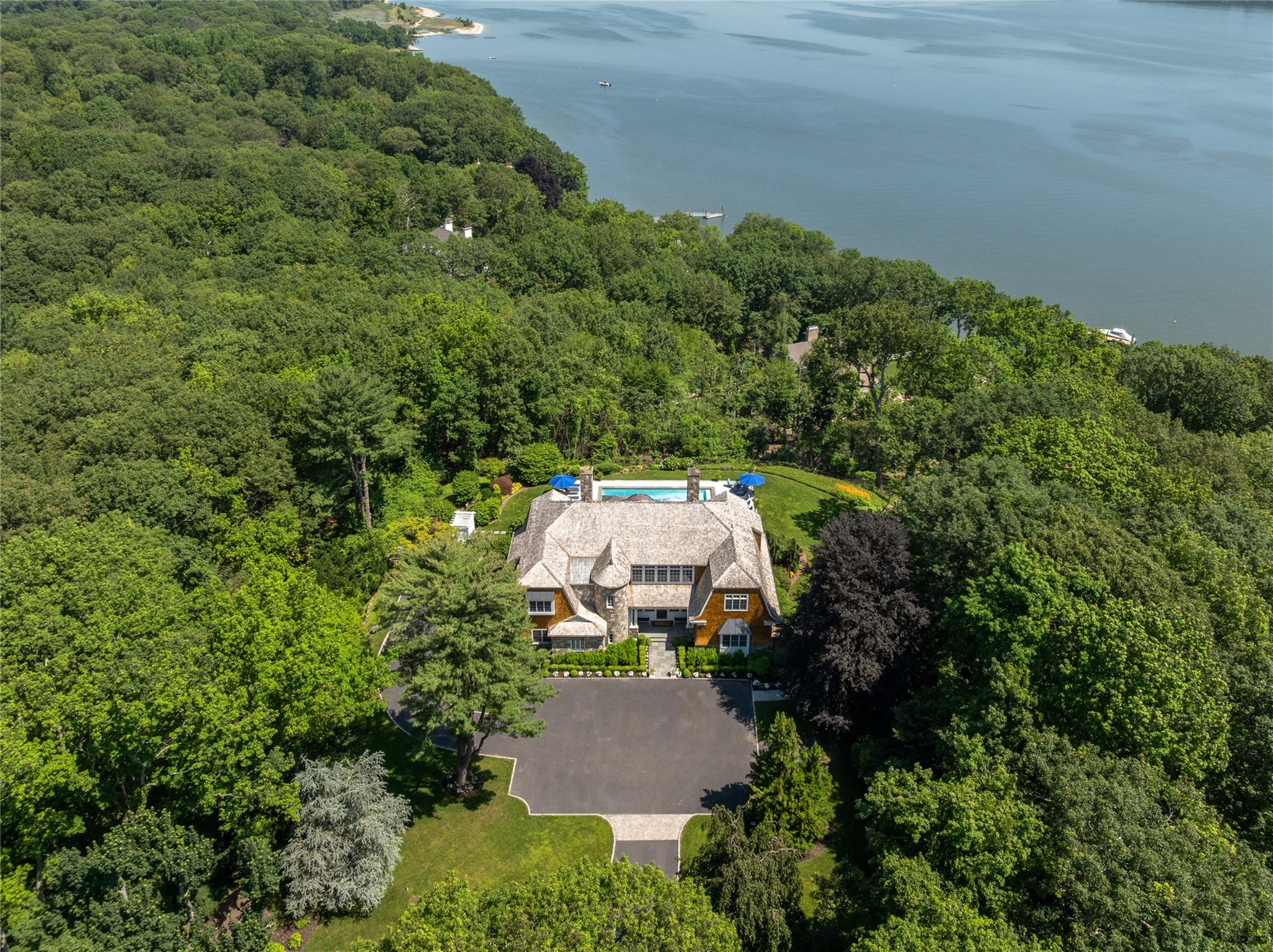 Introducing a truly exceptional waterfront estate nestled along the prestigious coast of Laurel Hollow, NY. Approached via a tree-lined driveway and set on 4.2 professionally landscaped acres, this Hamptons-style shingle and stone Colonial offers sweeping views of the glistening harbor from nearly every room and outdoor space. One of the home’s most distinctive features is its private mechanical tram - one of the only ones in the area - providing effortless access to a stunning Dock House with a kitchenette, just steps from your own sandy beach and deep-water dock.

Originally constructed in 2005 and thoughtfully redesigned, this North Shore masterpiece features intricate hardwood floors, oversized windows, and a dramatic double-height entryway that sets the tone for the luxury within. Spanning three levels and serviced by a private elevator, the home offers 4 spacious bedrooms and 5.5 designer bathrooms.

The open-concept layout is anchored by a striking bespoke bar with an illuminated countertop, alongside a gourmet center island kitchen equipped with chef-grade appliances and a walk-in pantry. Two impressive floor-to-ceiling fireplaces frame the dining and living areas, which seamlessly extend to a full-length teak deck overlooking the meticulously landscaped grounds and tranquil shoreline. There is also a wet bar / built-in coffee station and a cozy den that provides a warm and inviting extension of the main living space.

The Owner’s Wing is a luxurious retreat, accessed through double doors and featuring multiple walk-in closets, a spa-inspired ensuite bathroom, a fireplace, and French doors that open onto the second-story deck. Each additional bedroom includes its own ensuite bathroom. The first floor also offers a second den/flex space adjacent to a wet bar with a wine refrigerator, which leads directly to the outdoor entertaining area.

Additional amenities include a 3-car attached garage with a car lift, a large laundry room with a convenient chute, and a finished lower level complete with a lounge space and a matted gym. Outdoor living is equally impressive, featuring an oversized covered bluestone patio, a heated in-ground pool, and an outdoor shower.

This is a rare opportunity to own a one-of-a-kind coastal sanctuary that seamlessly blends luxury, privacy, and natural beauty in one of Long Island’s most coveted waterfront enclaves.