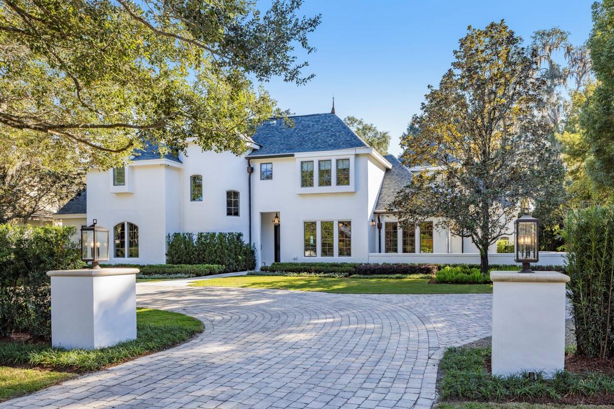 Along one of the cobblestone brick streets in the prestigious Via’s of Winter Park, this completely renovated residence pairs timeless European influence with clean architectural lines and bespoke finishes throughout. A circular driveway and manicured grounds designed by Signature Landscapes create a graceful approach. Inside, a dramatic curved staircase crowned by a breathtaking 1960s vintage Venini chandelier immediately sets the tone for the exceptional craftsmanship carried throughout the home. The main gathering room is striking and inviting, defined by vaulted ceilings, a Sequoia leathered stone fireplace hearth, and a wall of glass sliders that open seamlessly to the covered lanai and heated saltwater pool. The connection between indoors and out is effortless, designed for year-round entertaining and relaxed daily living, enhanced by a full outdoor audio system. A light-filled breakfast room sits just off the kitchen, offering an intimate everyday dining space. At the heart of the home, the custom kitchen is a showpiece. Naica leathered stone countertops and a waterfall island are complemented by custom cabinetry extending to the ceiling, a professional-grade appliance suite featuring Sub-Zero and Wolf, and convenience of two Miele dishwashers. Directly adjacent, the pantry mirrors the kitchen’s cabinetry and craftsmanship and features a built-in coffee station, seamlessly connecting to the laundry area and three-car side-entry garage. A beautifully appointed guest powder room with an integrated sink is thoughtfully positioned nearby. A separate lounge showcases a custom wet bar highlighted by dramatic stonework and an integrated sink, an elegant setting for conversation and evening gatherings. A dedicated office positioned just outside the primary suite features a wall of floor-to-ceiling shelving, cabinetry and file drawers. The primary suite serves as a private sanctuary, enhanced by vaulted ceilings, backyard views and a stately two-sided stone fireplace shared with the office. Two custom walk-in closets provide exceptional storage, while the spa-inspired bath showcases Taj Mahal leathered stone countertops with integrated dual sinks, a soaking tub and an oversized glass shower with dual showerheads. Upstairs, four additional bedrooms with custom closets are complemented by beautifully finished baths and a loft sitting area with hallway built-ins. Two of the bedrooms and a bath may be closed off to create a private suite, ideal for guests or multigenerational living. A secondary staircase leads to an impressive media room equipped with a 98-inch television, state-of-the-art 7.1 surround sound and extensive storage. Outdoor living is equally elevated, featuring a weathered marble pool deck, dedicated pool bath, newly installed summer kitchen with Coyote gas grill, hood vent, sink, and leathered stone counters and backsplash, plus an outdoor living room anchored by a two-sided fireplace and television. Modern systems include a Lutron lighting system on the main level, ADT alarm, security cameras throughout and a whole-home natural gas generator. Every element of this residence has been newly installed and custom-designed, resulting in a home that blends sophisticated design, advanced functionality, and exceptional spaces for intimate living and grand entertaining. From custom millwork to curated stone selections, this home reflects uncompromising quality and thoughtful design.