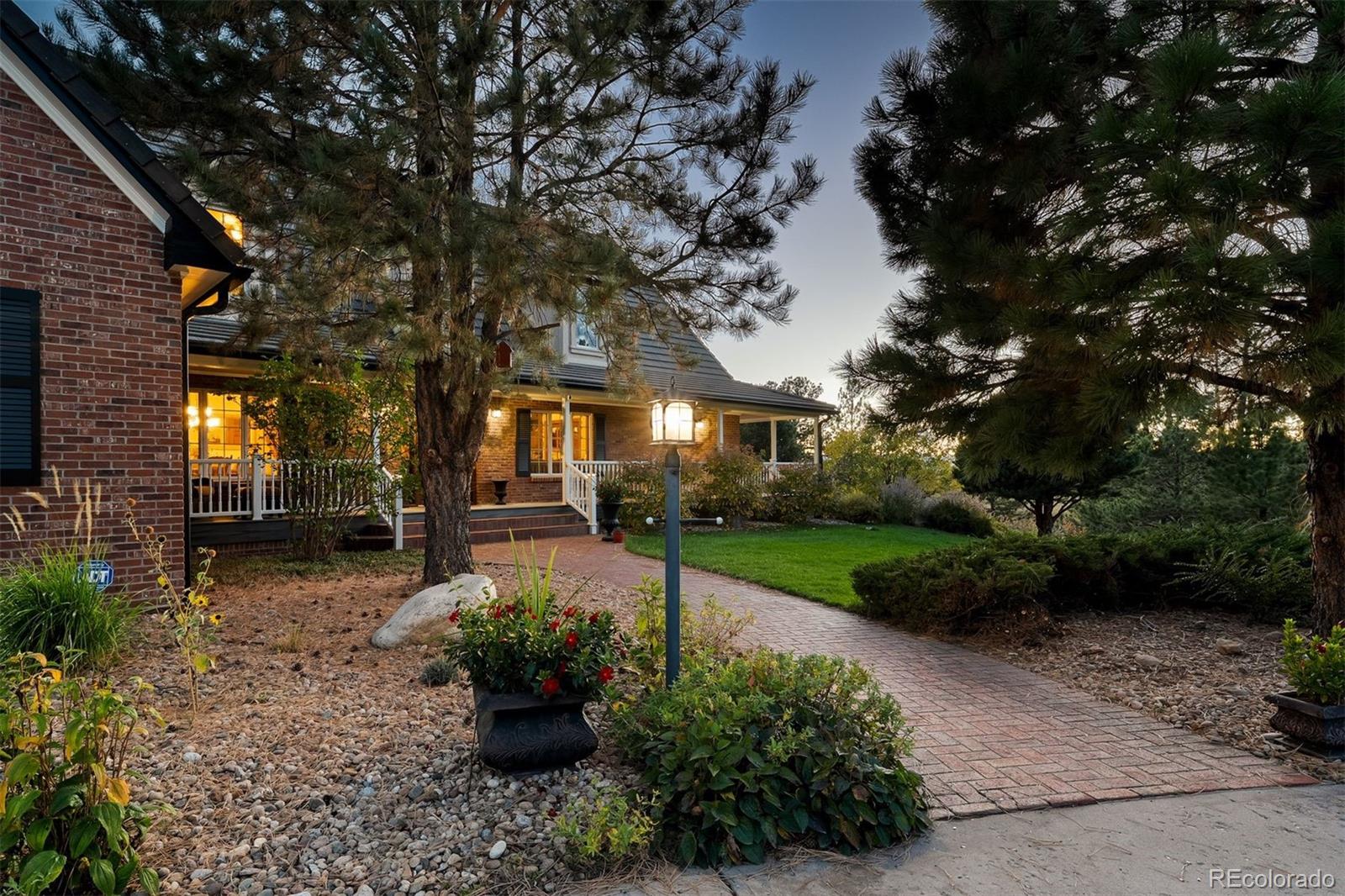 From a sweeping wrap-around porch, take in the tranquility of five wooded acres and a rolling meadow, a daily invitation to slow mornings and Colorado sunsets. Dormer rooflines and a classic brick facade emerge through mature trees, setting the tone for a home rich in character and warmth. Cherished by only two owners, this Butterfield neighborhood gem sits on a corner cul-de-sac lot, offering exceptional privacy, low traffic, and easy access to everyday amenities. The main level offers an open great room centered on a two-sided brick fireplace. Vaulted ceilings, expansive windows, and mountain views fill the space with light, while a wet bar elevates every gathering. The remodeled kitchen features generous cabinetry, a large center island, granite countertops, Bosch appliances, and seamless flow to two dining areas, ideal for both casual living and elegant entertaining. The main-level primary suite is a true retreat, featuring a separate sitting area, a two-sided fireplace, and deck access. The ensuite bath offers a timeless clawfoot tub, wainscoting, and a generous walk-in closet. Upstairs, an open loft with workspace supports everyday routines, while oversized bedrooms, including one with a private ensuite, offer flexibility. A large bonus room adapts beautifully as a media room or playroom, and a main-level office behind French doors adds versatility. The walk-out lower level features a spacious recreation room warmed by a wood-burning stove, a dedicated home gym, ample storage, and a bedroom suite with its own laundry, perfect for guests or multigenerational living. Outdoor living shines with a wrap-around Trex deck, a covered lower patio with hot tub and gas fire pit, a separate wood-burning fire pit, and a fenced garden area. An oversized three-car garage and circular drive complete the picture. Minutes from Colorado Golf Club, Centennial Airport, and DIA, this is a home that lives comfortably, hosts beautifully, and offers a true sense of place.