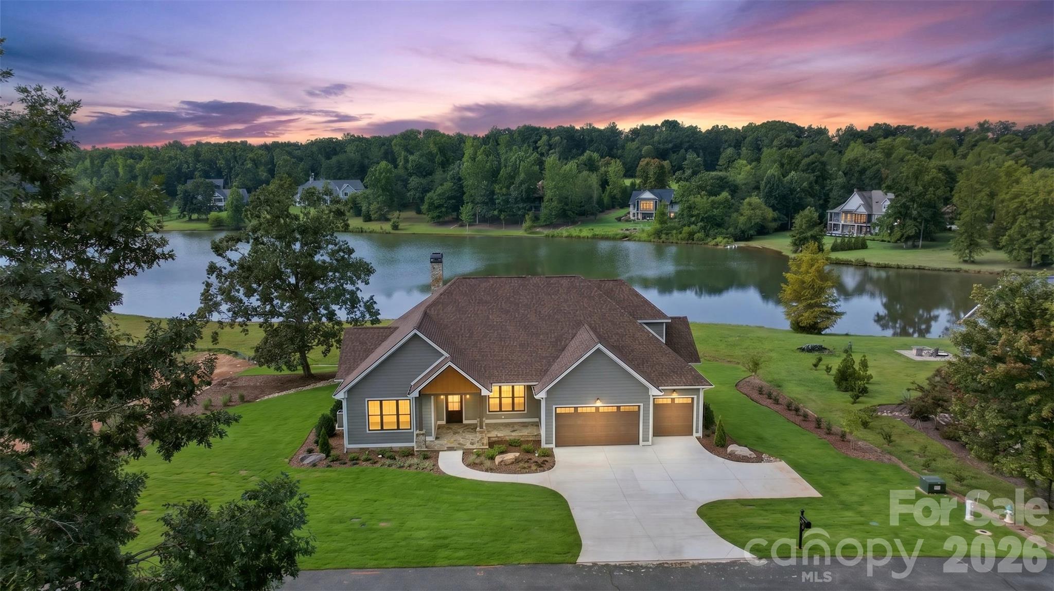 Lakefront living finds its finest expression at 966 Mapleton Lane, a new construction residence in the Derbyshire community of Columbus, NC. Four bedrooms, two full baths, and two half baths are set against a backdrop of 5-inch red oak hardwood, custom shaker-style cabinetry and vanities, and a Marvin Elevate window and door package. GE Café appliances anchor the kitchen, while the living room centers on a 42-inch fireplace configured for either natural gas or wood. In the primary suite, a custom tile shower, freestanding soaking tub, and bespoke closet storage by Carolina Closets complete a retreat of quiet comfort. Outdoors, the covered rear deck draws the lake into daily life, finished in Trex decking with custom cable railing beneath a tongue-and-groove cypress ceiling. A flagstone front porch, crowned by a matching cypress ceiling, offers a gracious arrival, framed by professionally installed landscaping and a full irrigation system. LP SmartSide siding, stone veneer at the foundation, CertainTeed Landmark architectural shingles, and custom 6-inch gutters with round downspouts give the exterior its enduring character. The three-car garage is appointed with epoxy-coated flooring and Haas doors with LiftMaster openers. Thoughtful practicalities follow throughout: custom closets by Carolina Closets, a GE washer and dryer, a Rinnai natural gas tankless water heater, generous attic storage, a fully encapsulated crawlspace with commercial dehumidifier, and a preinstalled generator connection. Water service is provided by Inman-Campobello Water District, complemented by an individual septic system and high-speed fiber internet through Windstream. A rare chance to pair the ease of new construction with the beauty of the lake