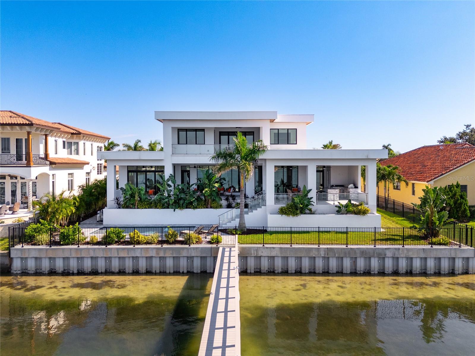 Introducing a Contemporary Waterfront Masterpiece in Tampa Bay. Striking modern architecture and clean, minimalist design come together in this extraordinary custom-built waterfront residence. Completed in 2023, this home makes a bold statement with its commanding curb appeal, soaring 28-foot entry, and dramatic 23-foot foyer. Brilliant natural light, soaring ceilings, and meticulous craftsmanship set the stage for a refined coastal lifestyle.The open-concept floor plan highlights a chef’s dream kitchen with custom cabinetry, pearl-white quartz island, Thermador appliances, gas cooking, full-height wine chiller, and built-in espresso machine, complemented by a discreet butler’s pantry. Expansive living and dining areas open seamlessly to the water, while the executive-style office and designer guest bath add both elegance and function.The owner’s suite is a private sanctuary with breathtaking views, balcony access, dual walk-in closets, and a spa-inspired bath featuring custom vanities, a Jacuzzi soaking tub, and a glass-enclosed multi-head rain shower. Upstairs, two additional en suite bedrooms and a large media room extend to a 330-square-foot covered terrace with commanding views of the bay.Outdoor living is elevated with over 1,200 square feet of covered waterfront terraces, a resort-style pool and spa, outdoor kitchen, and lush landscaping. Waterfront amenities include an updated seawall, large composite dock, kayak/paddleboard launch, boat lift, and mooring capacity for a sizable yacht.Located just ten minutes from downtown St. Petersburg and six minutes from the Gulf beaches, this residence offers an extraordinary blend of serenity and convenience. Nestled within the highly coveted, gated enclave of Bayway Isles, the community is distinguished by its 24/7 guarded security, pristine surroundings, and enduring sense of privacy.This estate is not simply a residence but a testament to vision, artistry, and uncompromising craftsmanship. More than a home—it’s a statement of modern luxury and life without compromise. Arrange your private showing today and experience the pinnacle of waterfront living.