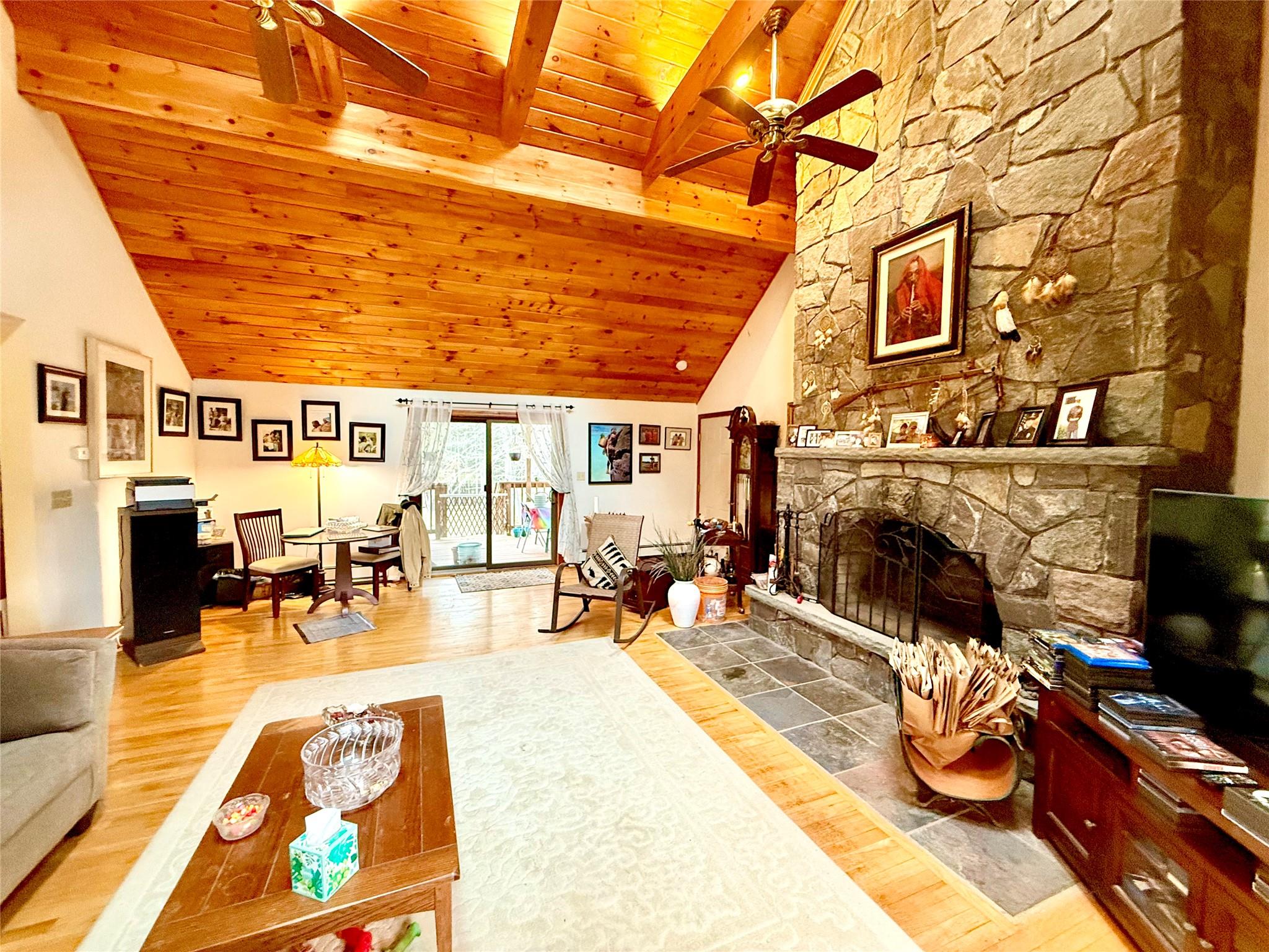 Living area with wood ceiling, wood finished floors, a stone fireplace, and ceiling fan