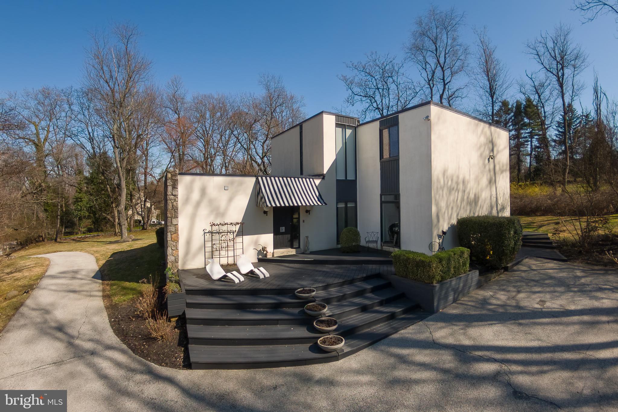 First time on the market since its custom construction in 1973, this striking four-bedroom, three-and-a-half-bath contemporary residence is sited on a beautifully elevated 1.07-acre parcel in Villanova’s coveted Lower Merion Township, tucked along a quiet double cul-de-sac.Wide, terraced steps lead to a handsome foyer where lacquered black hardwood floors immediately set the tone. Owned and designed by a professional interior designer, the home is a confident study in black and white—highly styled, yet grounded by an abundance of oversized windows that flood the interiors with natural light and draw the surrounding landscape inward.To the left of the foyer, a sunken den offers a welcoming retreat, complete with custom shelving and an en-suite bath—ideal for intimate conversation, a private office, or gracious guest accommodations. To the right, the expansive family room features 9½-foot ceilings, custom windows, and sliding doors that open to the rear terrace, creating an easy flow between indoor and outdoor living. This space connects seamlessly to the breakfast room and kitchen beyond.The kitchen is both sophisticated and highly functional, anchored by a black granite island with cooktop, double Dacor wall ovens, stainless steel refrigeration, and thoughtfully designed cabinetry. Generous storage throughout the kitchen and breakfast area ensures everyday convenience with everything close at hand.Through a wide cased opening, the dramatic dining room offers flexibility for two distinct seating areas. Long horizontal windows and a stylized feature wall add architectural interest and depth. Just beyond, a more formal living space is centered around a wood-burning fireplace, creating a warm and elegant gathering place. A beautifully appointed powder room completes this level.A circular staircase leads to the second floor, where three spacious family bedrooms—each with ample closet space—share a timeless hall bath finished in classic white tile with a tub and shower. The primary suite is a true retreat, featuring custom-built closets flanking the bed wall and additional bespoke cabinetry designed to discreetly house a television and provide extra storage. The spa-like bath includes a double vanity with glass vessel sinks, a separate water closet, and a dramatic wet room with custom tub and shower. Refined finishes and a skylight continue the home’s theme of light and connection to the outdoors. The conveniently located laundry sits just steps from the primary suite.A full lower level offers abundant storage and the opportunity for future finishing to suit additional recreational or living needs.Architecturally distinctive and thoughtfully designed, this Villanova contemporary offers privacy, light, and enduring style in an exceptional setting.