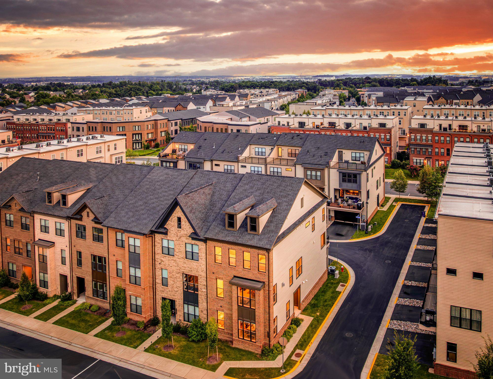What we have loved most about living here is how easy everyday life feels. We can walk to Brambleton Town Center for dinner, coffee, the library, shopping or a movie at Regal, then come home to a house that feels bright, open and incredibly comfortable for both everyday living and entertaining. Being an end unit makes such a difference. The extra windows along the side bring in so much natural light that you never feel boxed in, and with high ceilings, wide plank flooring throughout every level, hardwood stairs, contemporary aluminum railings and no carpet anywhere, the entire home has a clean, modern feel. The main level is where we spend most of our time, with the kitchen, dining and family rooms all flowing together so everyone can be in the same space without feeling crowded. The kitchen is exceptionally large, with 42-inch gray shaker cabinetry, upgraded quartz countertops, stainless steel appliances, a French door refrigerator, double wall ovens, gas cooktop with vented hood, pendant lighting over the island and one of our favorite features, a huge window over the sink with a wide panoramic view. The family room is anchored by a modern stone fireplace with a horizontal gas insert, while the formal dining area gives you plenty of space for larger dinners and holidays. On the other side of the kitchen, the rear deck almost feels like another room because of its size, with more than enough space for grilling, dining outside and having friends over. There is also a powder room on this level. The entry level gives you even more flexibility with a generous bedroom behind double French glass doors that works beautifully as a guest room, home office or private work space, along with another stylish powder room, recessed lighting, a mudroom with built-ins and direct access to the two-car garage with an EV charger. Upstairs, the primary suite feels like a true retreat with two walk-in closets, both with custom closet systems, and a beautifully finished bath with an oversized seamless glass shower, built-in seat, dual showerheads including a rain head, dual-sink quartz vanity and upgraded tile. The two additional bedrooms are both comfortably sized and share another updated bath with the same modern gray cabinetry, quartz and upgraded tile finishes found throughout the home. Then there is the fourth level, which completely changes the way you can use the house. We think of it as the fun floor. There is a large rec room with recessed lighting, a third powder room, substantial attic storage and direct access to the rooftop sky terrace. It is one of our favorite places in the house, whether we are watching a game with friends, having a game night, sitting outside with a drink or staying out late under the stars. The home is only four years old and has thoughtful details everywhere, including custom shades, modern five-panel doors and consistent finishes from top to bottom. Just as important, Brambleton itself gives you a lifestyle that is hard to duplicate. There are five community pools, nearly 20 miles of trails, parks, playgrounds, sports courts and community events, with Hanson Regional Park, Beaverdam Reservoir and the Ashburn Recreation Center all close by. HOA services include Verizon Fios internet and TV, trash and recycling, and this home also benefits from lawn maintenance. Brambleton Town Center is only about a third of a mile away, Dulles International Airport is just over 7 miles, and One Loudoun and major commuter routes are all easy to reach. Add in the highly regarded school pyramid, and what we have enjoyed most is being able to have so much right around us while still coming home to a bright, spacious place that feels private, modern and genuinely easy to live in.