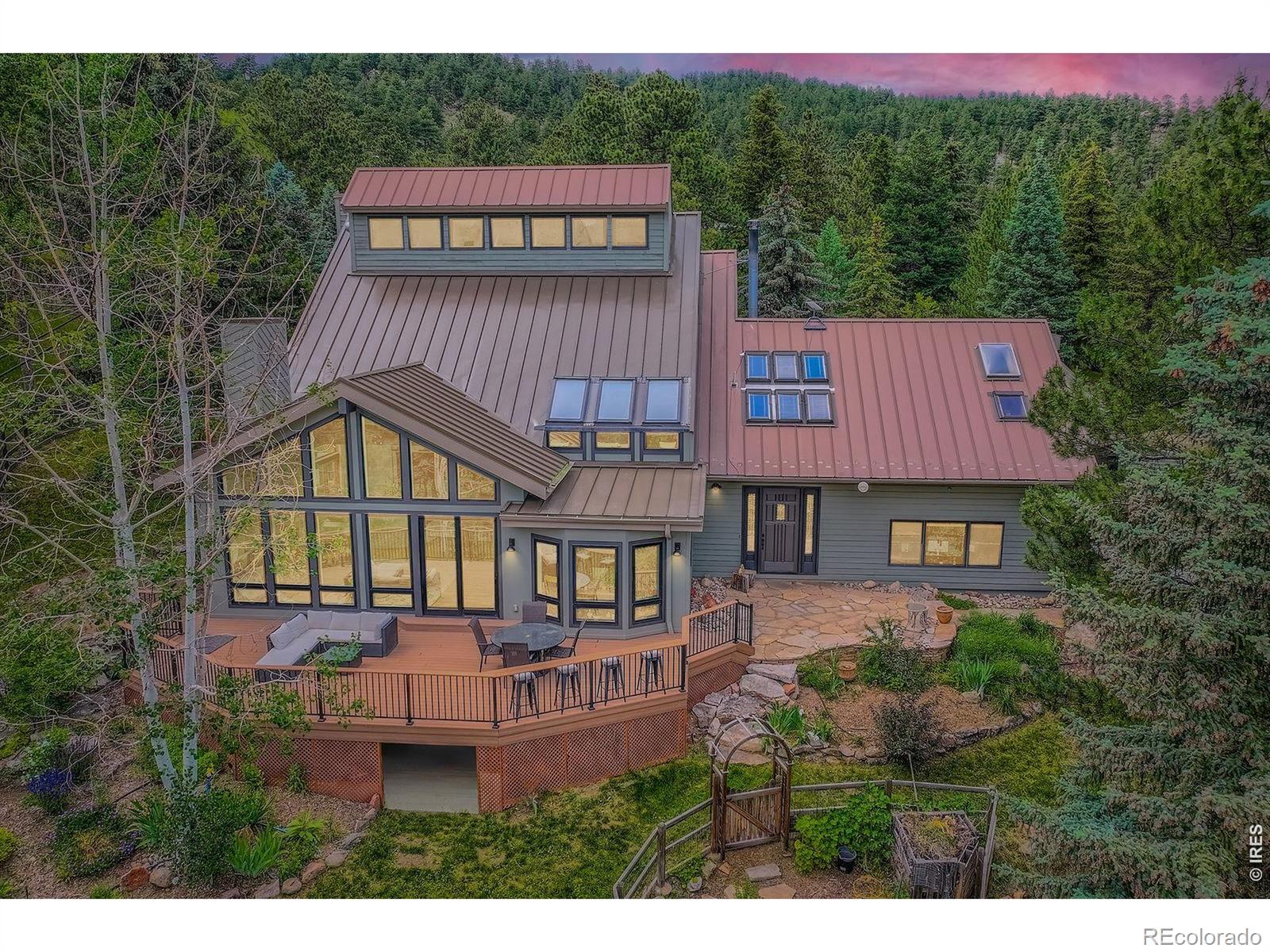 Beautifully renovated Sunshine Valley home, perfectly positioned on nearly two private acres just moments from Pearl Street Mall. Where elevated mountain living meets refined design: an exceptional five-bedroom home with a versatile bonus space, framed by sweeping views of Boulder and the plains below. Soaring, beamed ceilings and dramatic floor-to-ceiling windows anchor the great room, inviting natural light to pour in while capturing breathtaking vistas in every season. Rich wood and stone textures create a warm, alpine sophistication, blending timeless craftsmanship with an elevated aesthetic. The formal dining room, illuminated by a statement chandelier, sets the stage for unforgettable evenings against a backdrop of mountain skies. The eat-in kitchen is both functional and beautifully appointed, featuring a generous prep island, breakfast bar, and sunlit breakfast nook for effortless mornings and lively gatherings. A charming main-level bedroom with a wood-burning stove offers comfort and flexibility, ideal for guests or a private study. Ascend the handcrafted log staircase to a secluded upper-level retreat. The primary suite unfolds through a light-filled flex space, perfect for an office or wellness room, into serene sleeping quarters with dual closets, a wood-burning fireplace, and a Juliette balcony with stained glass overlooking a tranquil, tree-lined setting. The five-piece bath delivers spa-level indulgence with an oversized shower and soaking tub. Additional upper-level bedrooms include one with private deck access to the backyard sanctuary, while the top level offers a fifth bedroom plus a non-conforming sixth, ideal for guest quarters, creative space, or a studio. Outdoors, a fenced yard and flourishinggarden complement the natural landscape, creating a setting that feels both expansive and intimate. Just minutes from downtown Boulder's vibrant downtown, this rare offering delivers privacy, scale, and proximity-an extraordinary mountain estate.