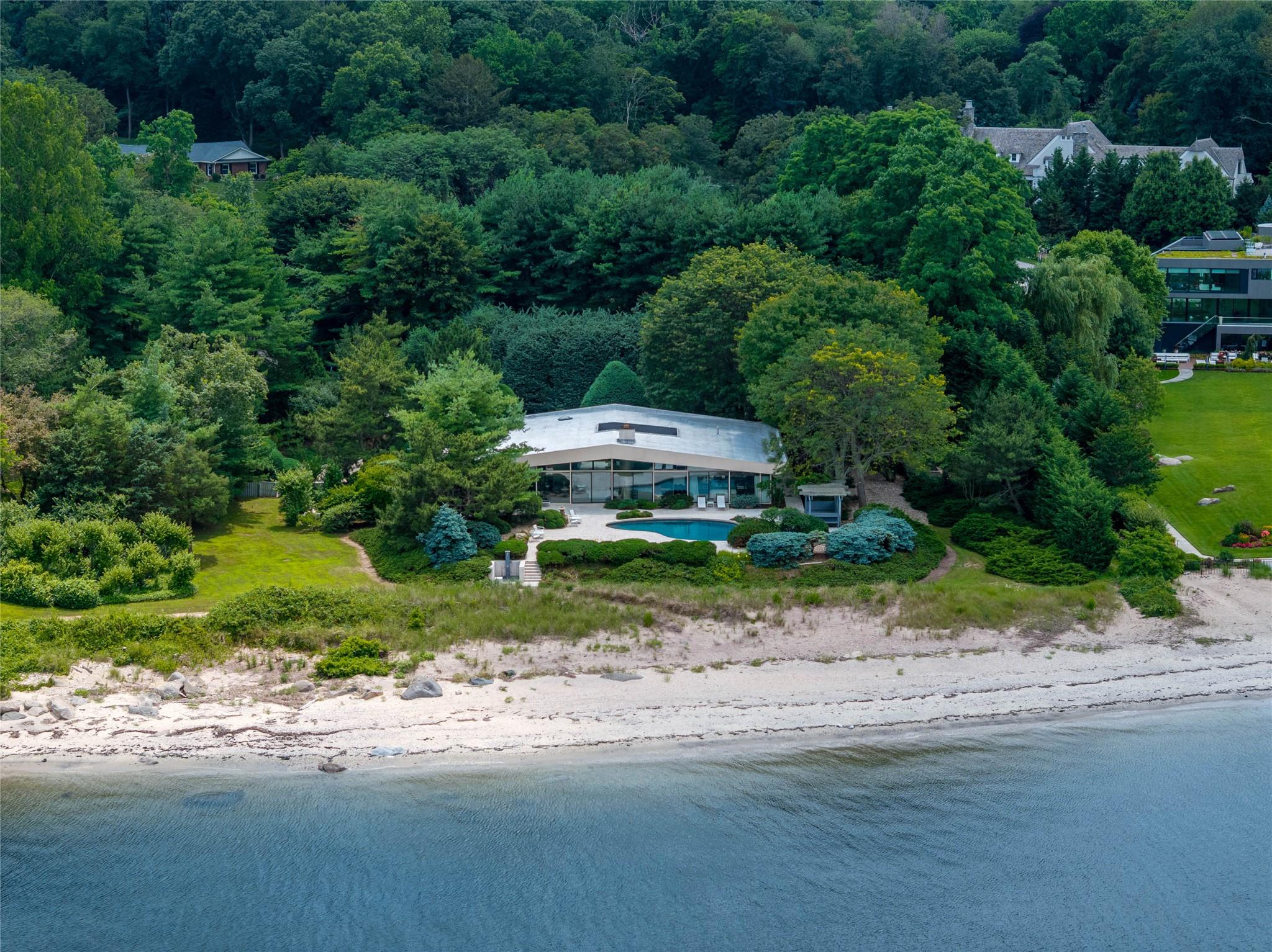 Set on over two acres of pristine waterfront along the shoreline of Sands Point, this custom-built contemporary beach house, masterfully designed by award-winning architect Daniel Schartzman, is a true architectural masterpiece. Thoughtfully designed to embrace its breathtaking setting on the Long Island Sound, the residence features soaring walls of glass and oversized windows that bathe the interiors in natural light while capturing uninterrupted water views from nearly every angle. A timeless work of art, the home showcases exceptional design elements including cedar-paneled ceilings, a bamboo front door, natural travertine-clad walls, grasscloth wallpaper, and a sculptural curved double-sided fireplace that anchors the open living spaces. At the heart of the home lies a stunning glass-enclosed conservatory - blurring the lines between indoors and nature - creating a tranquil centerpiece that sets this residence apart.

This residence has 4/5 bedrooms, 3.5 custom bathrooms, and an attached garage. The main-level primary suite opens directly to a serene waterfront terrace through sliding glass doors. Each bathroom is exquisitely appointed with bespoke vanities, intricate tilework, and beautiful stained glass windows. Seamless floor-to-ceiling storage solutions throughout the home contribute to its clean, minimalist aesthetic.

Outdoors, a sprawling sun-soaked patio provides the perfect setting for both relaxation and entertaining, leading to a private sandy beach and a sunken outdoor shower - an ideal touch for rinsing off after a day by the water. Additionally, a resort-style in-ground pool with a cascading waterfall feature enhances the outdoor experience, while a spacious pergola offers a shaded retreat to take in the sweeping coastal panorama. The home is framed by a round pebble driveway and lush, manicured landscaping, creating a picture-perfect setting. A gated entry courtyard provides a dramatic sense of arrival, unveiling a stunning walkway that leads through the conservatory and on to the front entrance. Meticulously maintained and masterfully designed, this waterfront haven represents the pinnacle of elevated coastal living.