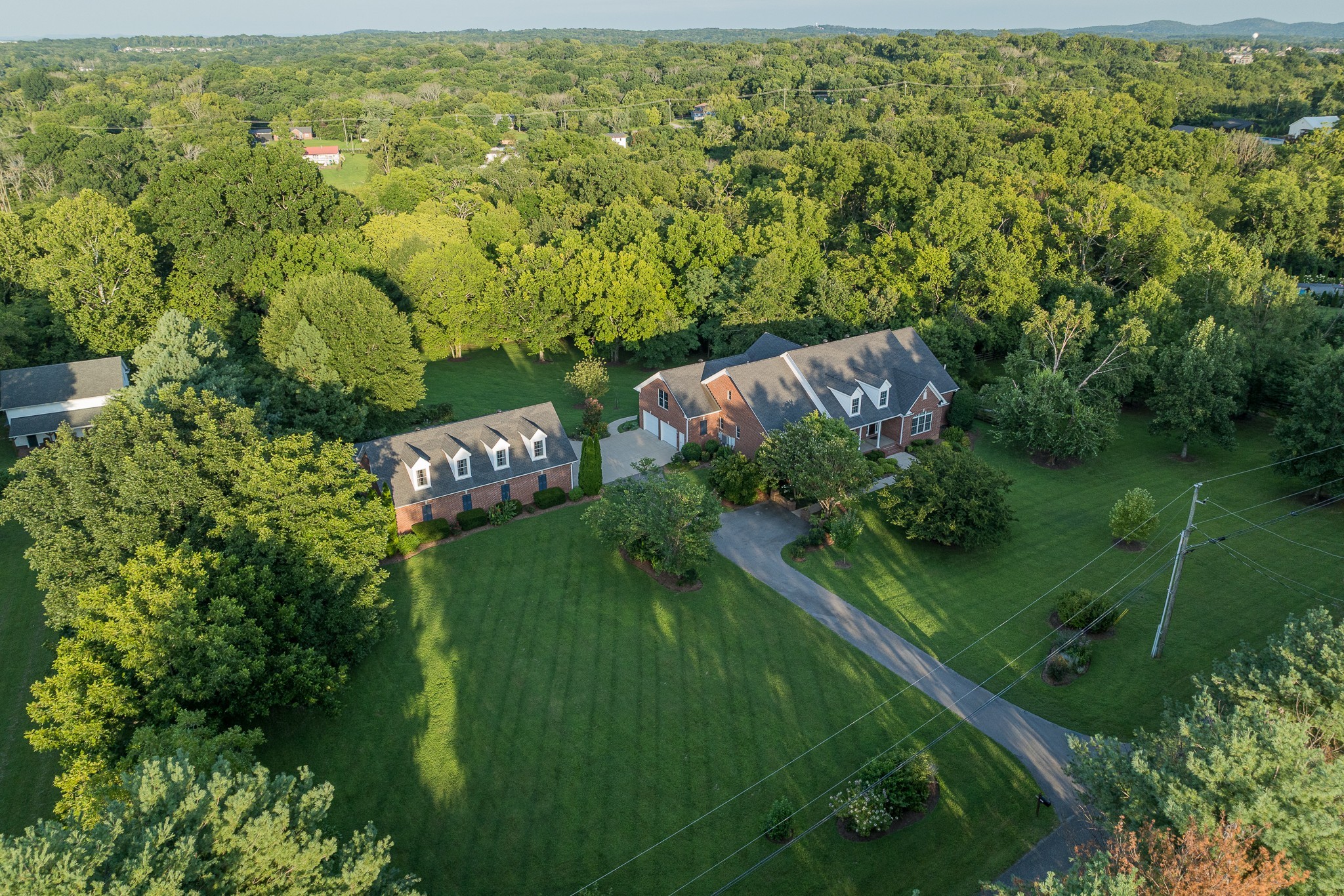 One address, three compelling possibilities: a luxury residence, flexible multigenerational retreat, and workshop/collector compound. On 5.1 private, wooded acres, the all-brick home provides 8,989 heated and cooled square feet per prior appraisal, with 2 main-level suites and a 3,438-square-foot walk-out basement. A powered outbuilding/workshop adds approximately 3,300 square feet under roof for cars, equipment, hobbies and storage.Inside, a vaulted great room centers on a floor-to-ceiling stone fireplace and skylights. Separate living and dining rooms have coffered and tray ceilings. The kitchen includes granite counters, a 6-burner gas cooktop, double ovens, warming drawer, pot filler, 48-inch built-in refrigerator and casual dining area. The primary suite has built-ins, a walk-in closet, steam shower, garden tub and double vanities. A second suite completes the main level; upstairs are 2 bedrooms with private baths, a rec room and media room with refreshment area.Seven windows and French doors bring natural light into the walk-out basement, with 2 large living areas, a kitchenette without a range, an office, full and half baths, flex/work areas and substantial storage. Its separate exterior entrance opens to a covered lower patio beneath the upper porch.The full-brick detached building is equipped for serious use: 3 overhead doors, an air-conditioned workshop, 120/240V power, work sink, cabinetry, half bath, epoxy-coated floors and a fully decked upper level. A tall-clearance carport adds covered room for oversized vehicles or recreational equipment.Established trees, landscaping, gardens and covered outdoor spaces complete the setting. With no HOA and access to I-24, this is a compelling Greater Nashville alternative for buyers comparing acreage in Nashville, Brentwood, Nolensville, Franklin and Murfreesboro—or relocating to Middle Tennessee. Real privacy, flexible living and substantial workshop capacity come together in a way few properties can match.
