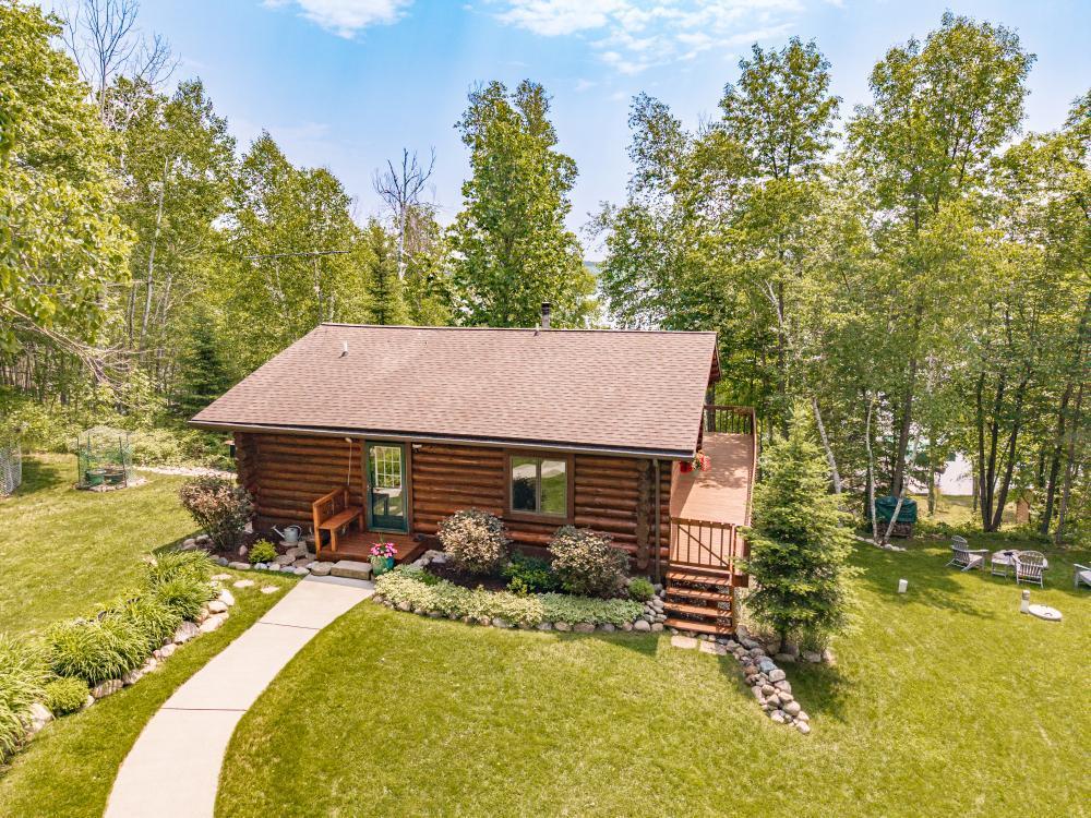 This stunning 2-bedroom, 2-bathroom log home is privately nestled in the woods on a peaceful 9-acre lot along the scenic shores of Balsam Lake. Surrounded by mature trees and natural beauty, it’s the perfect year-round getaway for those seeking tranquility and a connection to nature. Enjoy 226 feet of sandy lake frontage, a 12x8 boathouse, and a private VRDO 6-foot-wide dock—ideal for swimming, fishing, or relaxing by the water. Balsam Lake is renowned for its clear water, spanning 700+ acres and offering excellent fishing and paddling opportunities. It connects to Scrapper and Haskell Lakes, perfect for peaceful canoeing and kayaking. The property includes a 36x30 oversized Morton building with roughed-in plumbing and a separated concrete slab, offering potential for added living or workshop space. An overhang provides additional covered storage for gear and equipment. Outdoor enthusiasts will love direct access to miles of ATV and snowmobile trails and nearby Chippewa National Forest. The Mesabi Trail, a 150-mile paved biking route, is just 30 minutes away. Inside, the main-level living room features a Vermont Castings wood stove and ceiling fan, while the kitchen offers tile flooring, knotty alder cabinetry, a peninsula with breakfast bar, and natural light from a skylight. The adjacent dining room opens to a screened-in porch and refinished wraparound deck with stunning lake views. The main-floor primary bedroom offers vaulted ceilings, scenic views, and close proximity to a ¾ bath with walk-in shower and custom alder cabinetry. The lower level includes a second bedroom with private ¾ bath, a cozy family room with walkout to a 35x10 concrete patio, and a firepit area for relaxing evenings. A spacious laundry and storage area with lake access presents potential for a third bedroom with walkout. Recent updates include a new septic system (2022), ridge cap roof upgrade (2023), new basement lighting and ceiling tiles (2024), selective log repairs (2022), and a well-maintained exterior. Additional features include a Generac backup generator, Andersen doors and windows, and beautifully kept landscaping. Combining rustic charm, comfort, and outdoor adventure, this log home is the perfect lakeside escape.