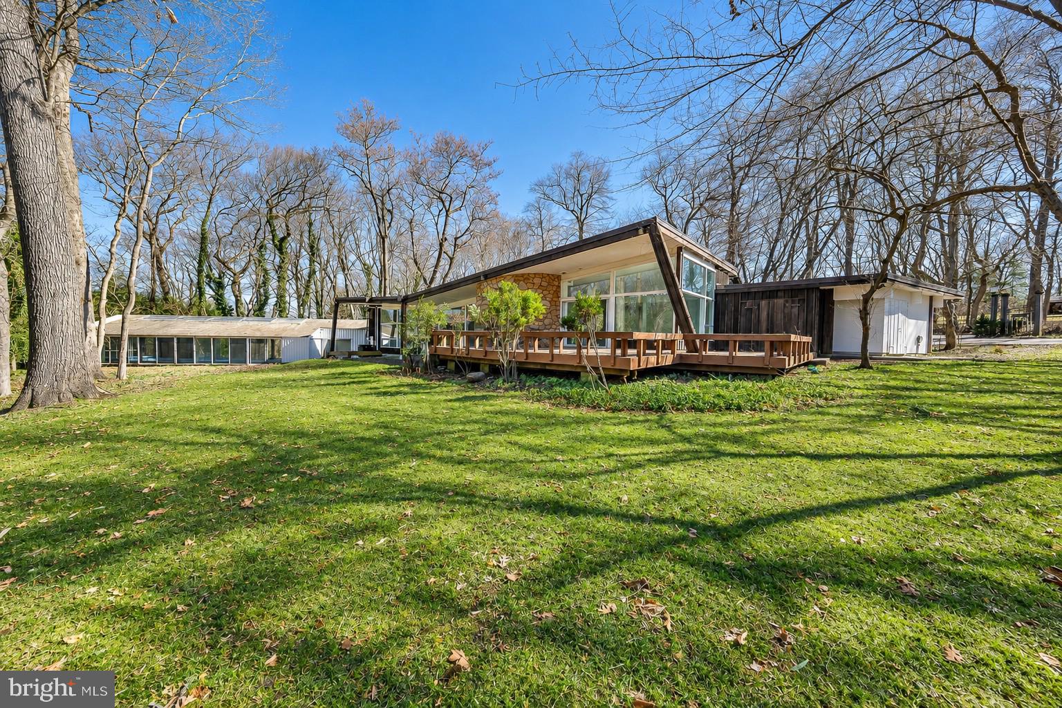 Located on one of Penn Valley’s most desirable streets, 39 Fairview Road is a distinctive historic mid-century modern residence surrounded by lush, mature landscaping that creates an exceptional sense of privacy and tranquility. Rich in architectural character, the home showcases thoughtful design elements throughout its expansive living spaces, beginning with a striking stone exterior, inviting front courtyard, and double carport accented by warm, natural tones. The entry opens to an impressive living room featuring new tile flooring, soaring ceilings, recessed lighting, dramatic floor-to-ceiling windows, a unique curved fireplace, and sliding glass doors leading to a spacious rear deck. The adjoining dining room is equally well suited for intimate gatherings or large-scale entertaining, with a high ceiling and direct access to a stone patio. The dining area flows seamlessly into the updated eat-in kitchen, creating an open and inviting entertaining space. The kitchen is designed for both everyday living and entertaining, featuring a large center island, high-end appliances, abundant cabinetry, a spacious breakfast area, and a wall of windows that fills the room with natural light. Two separate stone patios provide additional opportunities for outdoor dining and relaxation. A long corridor lined with generous closet space leads to the spacious primary suite, complete with three walk-in closets and an ensuite bathroom featuring a double vanity, soaking tub, and glass-enclosed shower. Sliding doors open to a peaceful private atrium, while an adjoining den or home office features a wall of built-in cabinetry. Five additional bedrooms offer excellent closet space and abundant natural light, including one with an ensuite bath, along with an additional full hall bathroom.The lower level provides flexible accommodations ideal for an au pair, guests, or an in-law suite, with a private bedroom and full bathroom. One of the home’s most remarkable features is the large indoor swimming pool, offering year-round enjoyment for lap swimming, recreation, or entertaining. The rear deck and multiple patios further extend the living space outdoors and provide wonderful settings for relaxing or gathering with family and friends. This exceptional property offers a rare combination of privacy, architectural character, generous living space, and endless possibilities. Located within the award-winning Lower Merion School District and convenient to shopping, dining, entertainment, major roadways, public transportation, and Center City Philadelphia. An additional opportunity exists to purchase the approximately 1.07-acre adjacent lot, providing the option to build a new residence, create a multi-generational compound, or expand the existing living space and grounds.