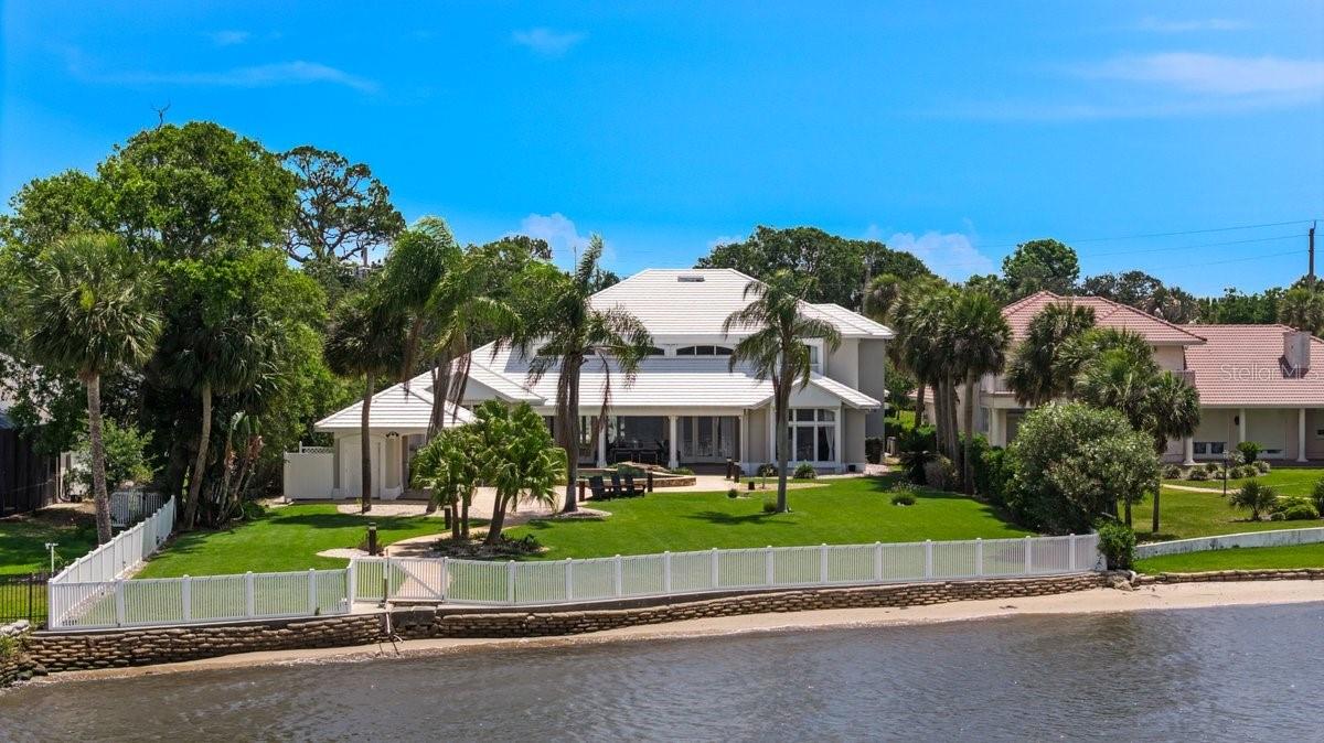 Virtually Staged. Welcome to a remarkable direct riverfront estate that embodies the very best of luxury coastal living in Ormond Beach. Situated on a beautifully landscaped half-acre homesite, this custom-built residence offers more than 5,300 square feet of thoughtfully designed living space, where expansive river views serve as the backdrop to everyday life. From the moment you arrive, the manicured grounds, stately entrance, and park-like setting create a memorable first impression and set the tone for the elegance found throughout the home. Inside, the residence unfolds with a spacious, light-filled floor plan designed to balance entertaining with comfortable daily living. The bright kitchen serves as a natural gathering place, featuring a generous eat-in dining area perfect for casual meals, morning coffee, or hosting family and friends. Rich wood flooring enhances the main living spaces, while soaring ceilings, walls of glass, and abundant natural light draw attention to the home's most impressive feature, its breathtaking riverfront setting. The grand living room is both welcoming and dramatic, offering panoramic water views that create a constant connection to the outdoors. Adjacent to the main living area, an expansive riverfront lounge provides an exceptional space for entertaining and relaxation. With ample room for gathering, stunning water views, and plumbing already in place for a future wet bar, this versatile space is perfectly suited for everything from intimate evenings to large-scale entertaining.The flexible floor plan offers five bedrooms plus a dedicated office, with three guest bedrooms thoughtfully located upstairs to provide privacy and separation from the primary living spaces. Whether accommodating extended family, working from home, or creating dedicated media and hobby rooms, the home offers exceptional versatility. A spacious three-car garage provides plenty of room for vehicles, recreational equipment, and all the essentials of an active coastal lifestyle. The first-floor owner's suite is a true retreat, thoughtfully positioned to maximize the tranquility of the riverfront setting. Expansive windows frame sweeping water views, creating a serene backdrop from sunrise to sunset. The luxurious ensuite bath features custom closet systems, a spacious walk-in tiled shower, and a soaking tub designed for relaxation. Private access to the lanai further enhances the suite's sense of seclusion, allowing for effortless access to the pool and outdoor living spaces. Outside, the property transforms into a private resort-inspired oasis. The custom pool is highlighted by stacked stone accents and multiple cascading waterfalls that add both visual beauty and soothing ambiance. A large covered cabana provides a comfortable gathering space, while the fully equipped summer kitchen makes entertaining effortless. Whether hosting elegant evening celebrations or enjoying a quiet sunset by the water, the outdoor living experience is nothing short of extraordinary. Beyond the property itself, the location is equally compelling. Nestled along one of Ormond Beach's most desirable riverfront stretches and just moments from the Atlantic Ocean, this exceptional address offers the rare combination of direct Intracoastal waterfront living and convenient beach access. Residents enjoy close proximity to local dining, shopping, and everyday conveniences while still experiencing the privacy, serenity, and beauty of a true waterfront retreat.
