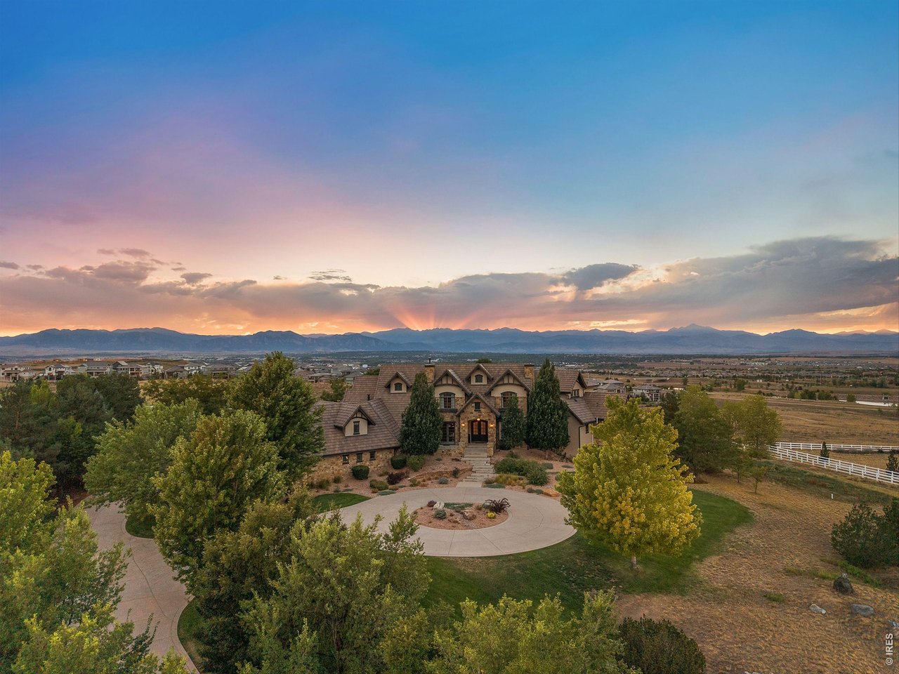 Perched atop one of Spruce Meadows' most coveted homesites, this remarkable custom residence commands sweeping 360-degree views of the Flatirons, foothills, and snowcapped back range. Backing to open space and oriented west, the property captures Colorado's landscape in every direction while offering exceptional privacy and generous grounds within an established neighborhood.Natural light fills the interiors, where thoughtfully placed windows frame the mountains beyond. A dramatic 20-foot great room is crowned with exposed beams and anchored by a soaring floor-to-ceiling rock fireplace. Walnut hardwood floors, hand-troweled walls, intricate millwork, and a sculptural staircase showcase the craftsmanship throughout. The chef's kitchen pairs custom cabinetry with premier Wolf and Sub-Zero appliances, including an eight-burner range, while the adjoining breakfast area opens effortlessly to the outdoor pavilion.Occupying a private wing of the main level, the primary suite features a fireplace, private balcony, and spa-inspired bath with soaring ceilings and a shower positioned to capture the views. A richly paneled study offers a distinguished home office. Upstairs, two bedroom suites each feature private baths, while a loft with an adjoining bath provides an ideal office, library, or optional 5th bedroom. An updated fitness studio sits above the oversized four-car garage.The walk-out lower level is designed for entertaining with a theater, full bar, fireside lounge, billiards area, and private guest suite. Outside, resort-inspired grounds feature a pool surrounded by expansive stone terraces, outdoor fireplace, fire pit, built-in grill, sport court, hot tub, and cold plunge-all set against a spectacular Front Range backdrop.Timeless architecture, remarkable privacy, and extraordinary views define this exceptional Mountain View Circle residence, ideally positioned with convenient access to Boulder, Denver, and DIA.
