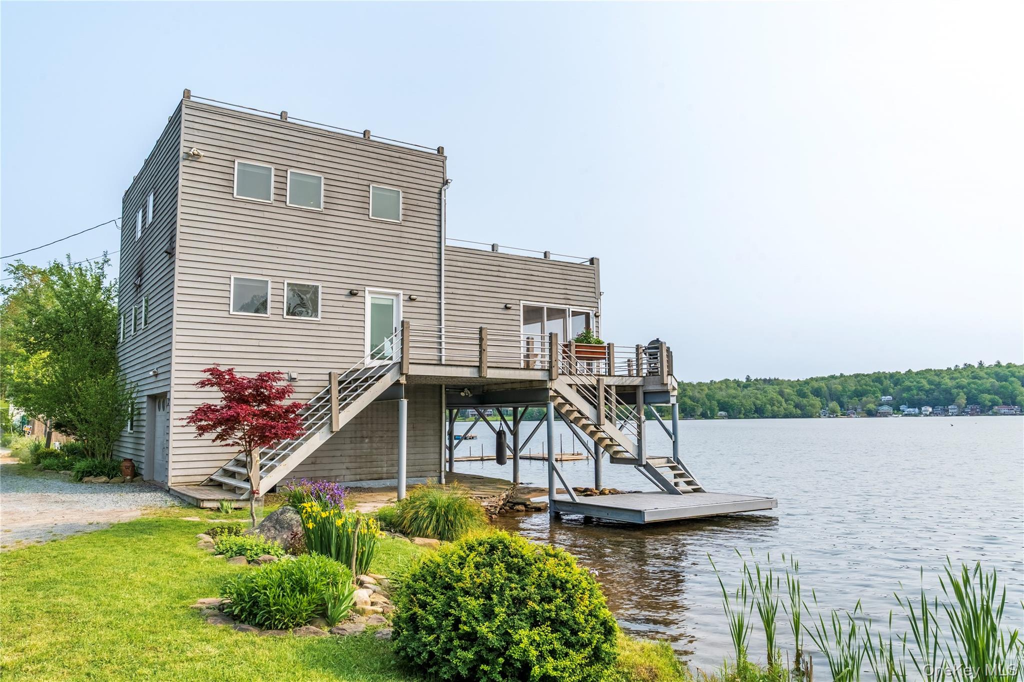 Minutes from Bethel Woods! EXCEPTIONAL lakefront living in Bethel, NY on White Lake / Kauneonga Lake. This contemporary waterfront retreat offers breathtaking panoramic lake views from nearly every room and is set directly on the water with a year-round dock, multiple sun decks, and a private shaded sandy beach. One of the few motor-boat lakes in Sullivan County! The open-concept main level features hardwood floors and seamless indoor-outdoor flow, with French doors from the living room to the main deck and additional access from the dining area to a screened-in porch overlooking the lake. A full bath and laundry hookups complete the main level. The upper level features a spacious primary bedroom with stunning water views, a private sun deck, and a mini-split A/C system. The fully finished lower level offers a second bedroom with propane stove and electric baseboard heat, a full bath, and a versatile approximately 350 sq ft bonus room currently used as a gym and sauna—ideal for a THIRD BEDROOM or additional sleeping area with direct walkout lake access. The exterior is enhanced by gardens, a shaded bluestone patio, and multiple outdoor entertaining spaces. Enjoy a vibrant lake lifestyle with boat-accessible restaurants, walkable dining, and one of the area’s most social motorboat lakes. Municipal sewer and private drilled well. A rare opportunity to own a true lakefront escape.