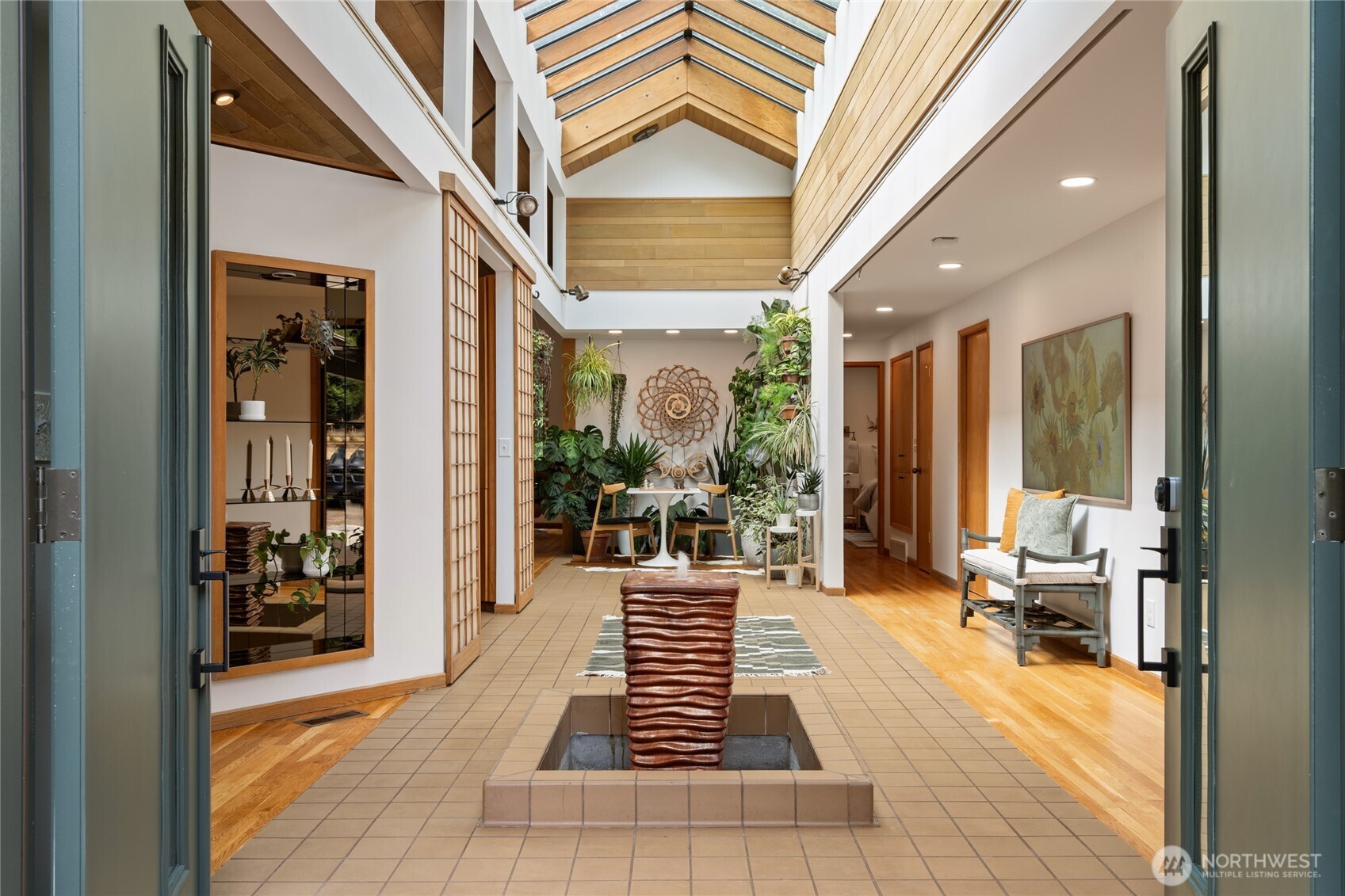 Truly one of a kind! Step into the dramatic skylight atrium & experience a home that perfectly blends iconic mid-century design with modern upgrades. Thoughtfully rebuilt, the owners refinished hardwood floors, preserved vaulted wood ceilings, and chose new fixtures to complement the mid-century modern style - like black floor-to-ceiling windows & a chic Malm fireplace. Major system updates include electric, plumbing, furnace, foundation, windows, new exterior paint, EV charging & a long-life metal roof. Fantastic layout with 4 beds, 4 baths, family room, flex spaces & tons of storage. There is truly room for everyone in this house! Set on nearly half an acre surrounded by trees, this exceptionally private sanctuary features sitting areas, garden beds, a greenhouse, lawn & huge Trex deck.