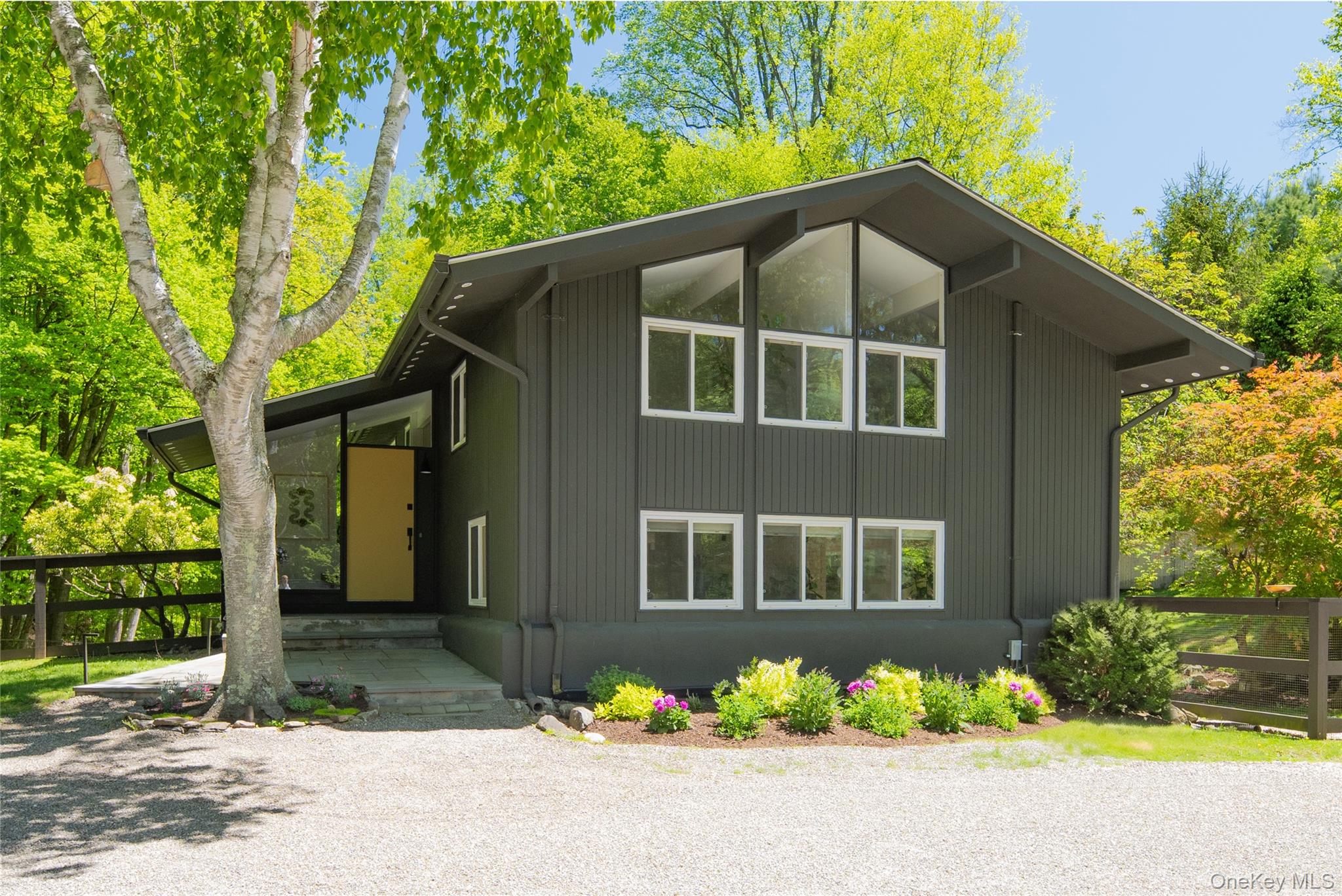 This midcentury retreat in the heart of Pound Ridge is sited on over three sprawling acres, featuring a light-filled 1966 post-and-beam main residence by architect Carl Koch and a detached, two-level, guest house. The main house (2,322 sq. ft.) fully remodeled, offers three bedrooms, three bathrooms, an open floor plan, beamed ceilings, and floor-to-ceiling walls of glass that span the first level. A classic brick fireplace with a raw bluestone floating hearth anchors the light-filled living space, which flows seamlessly into a newly remodeled kitchen appointed with custom cabinets and Fisher & Paykel appliances. An open dining area,  powder room bathroom and an office/pantry room complete the space. The second-level primary bedroom boasts oversized windows, exposed beams and a new spa-inspired bathroom with a large soaking tub and radiant heat flooring. Two generous bedrooms share an updated full hall bathroom. All bedrooms include new ductless a/c & heat units. A new Generac automatic whole-home generator services both the main house and guest house.The spacious, two-level guest house (870 sq. ft.) provides a complete living experience with white wide oak floors, a remodeled full bathroom, and a fully updated kitchen with new appliances & washer/dryer unit, French doors open to a private deck offering serene treetop views. The property is reached via a long driveway and is characterized by historic stone walls, level lawn spaces, and direct access to local nature trails. This architectural residence is located just minutes from Scotts Corners, convenient to the Merritt Parkway and Metro-North, and is approximately one hour from Manhattan.