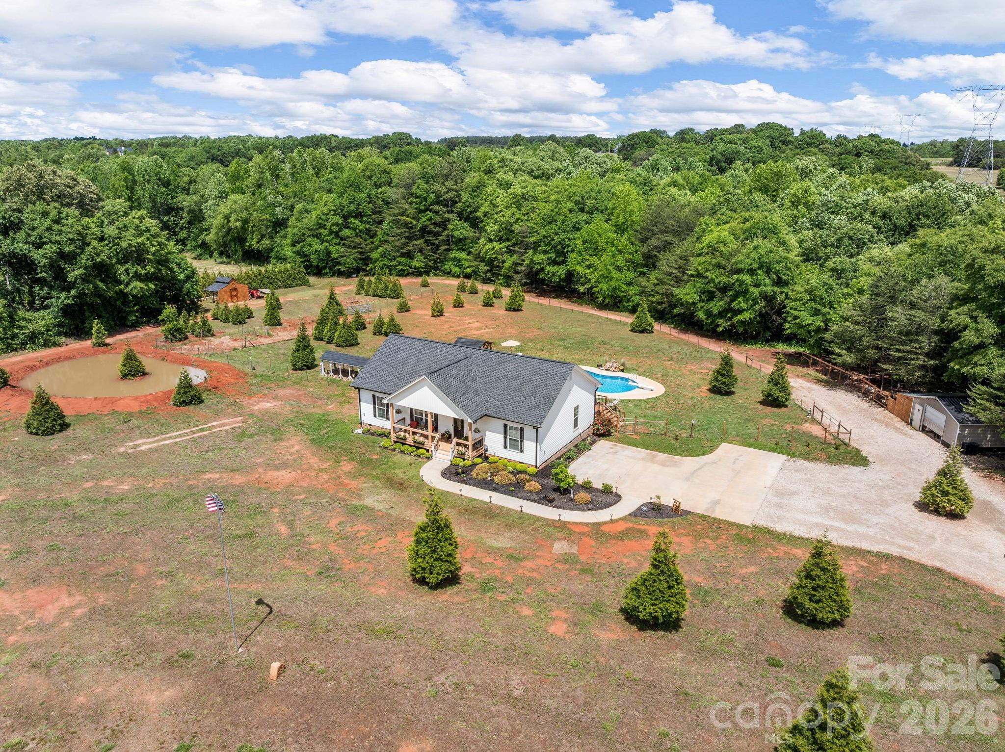 Some things take generations to build. This one's already done.Set on 7.21 acres along the banks of Buck Creek, 1076 McSwain Road is a modern homestead — built new in 2023, but designed for a life that looks a lot like the one you've been dreaming of. No HOA. No neighbors on top of you. Just land, water, and room to grow into whatever you need it to be.The fenced paddock, barn, chicken coop, and utility buildings are already in place, so you're not starting from scratch — you're stepping into something already humming. The creek runs along the edge of the property, and what lies beside it is open, usable acreage that rewards the imagination. Garden beds, more animals, future outbuildings — the land invites it.Inside, the home is smart and well-designed — lighting, thermostat, alarm, and cameras all controlled through an app or Alexa. The kitchen anchors the space with double ovens and an open flow into connected living areas. The primary suite is generous, with a garden tub, and the floor plan includes planned space for a future attached garage.The saltwater pool and covered pool house make the land livable in every season — a Sunday afternoon with family, a quiet evening after chores, a long weekend with friends. RV septic and electric hookups plus a dedicated pad mean guests and gear always have a place too.District 2 schools. Privacy without isolation. Creek frontage that never gets old.If you've been waiting for the right piece of land to start living differently, this is it.